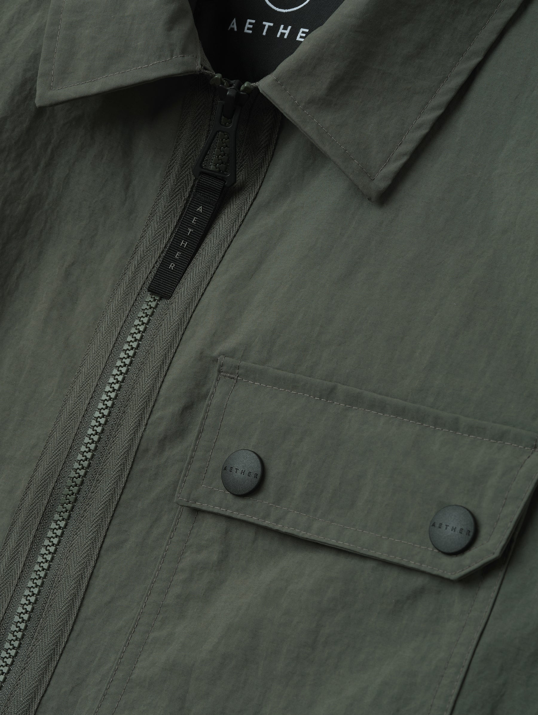 Closeup detailed view of the center-front zipper, collar, and dual-button chest pocket on the Landon Jacket in Saville Green from AETHER Apparel.