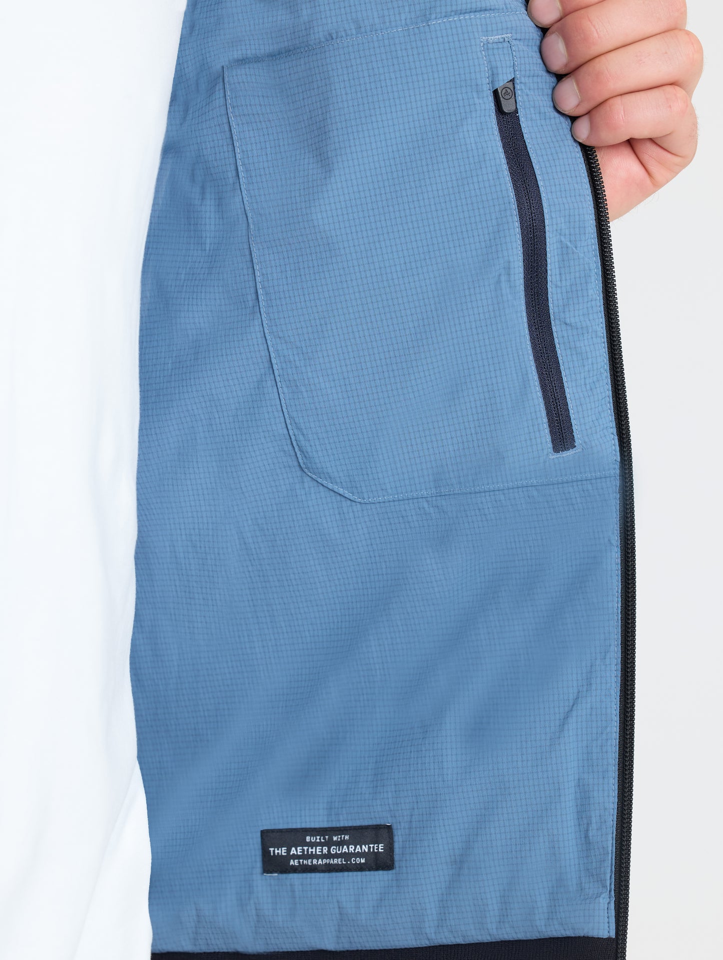 Closeup view of wearer's interior left zipped pocket of Prospect Packable Down Jacket in Portal Blue from AETHER Apparel.