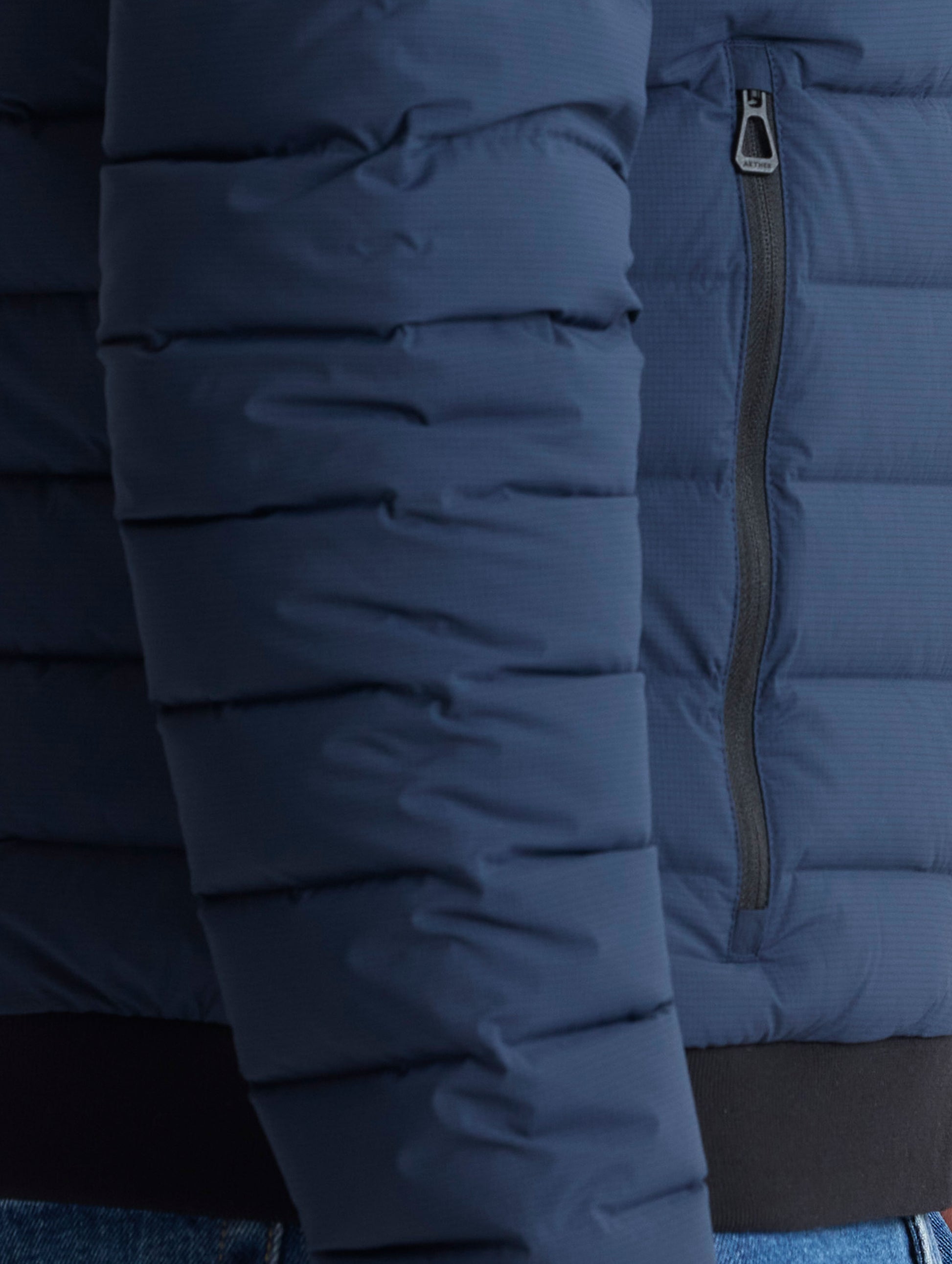 Closeup view of wearer's right zipped hand pocket of Launch Full-Zip Hooded Jacket in Total Eclipse dark blue from AETHER Apparel.