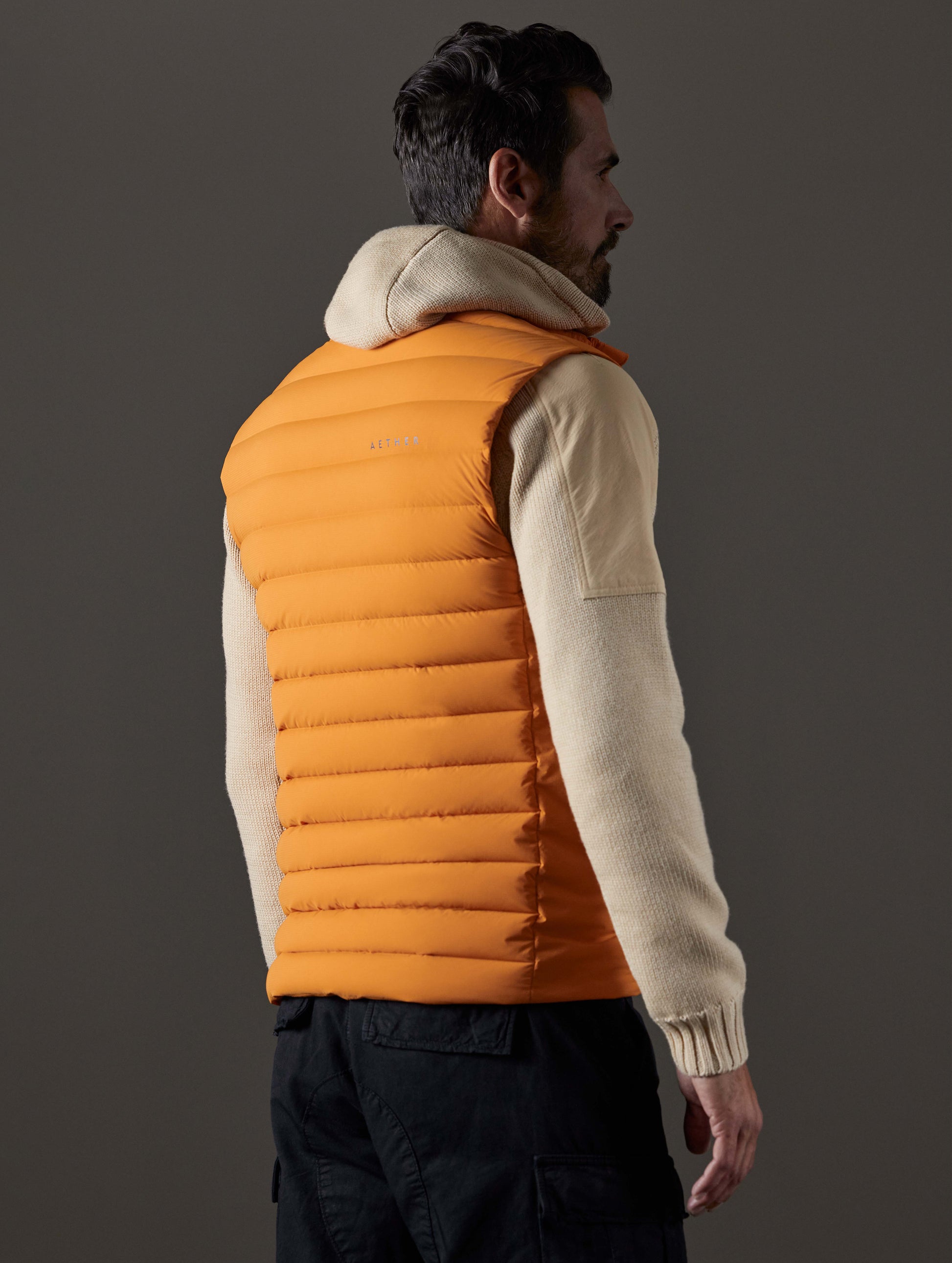 Rear 3/4 body view of man wearing Launch Vest in Midas Orange from AETHER Apparel.