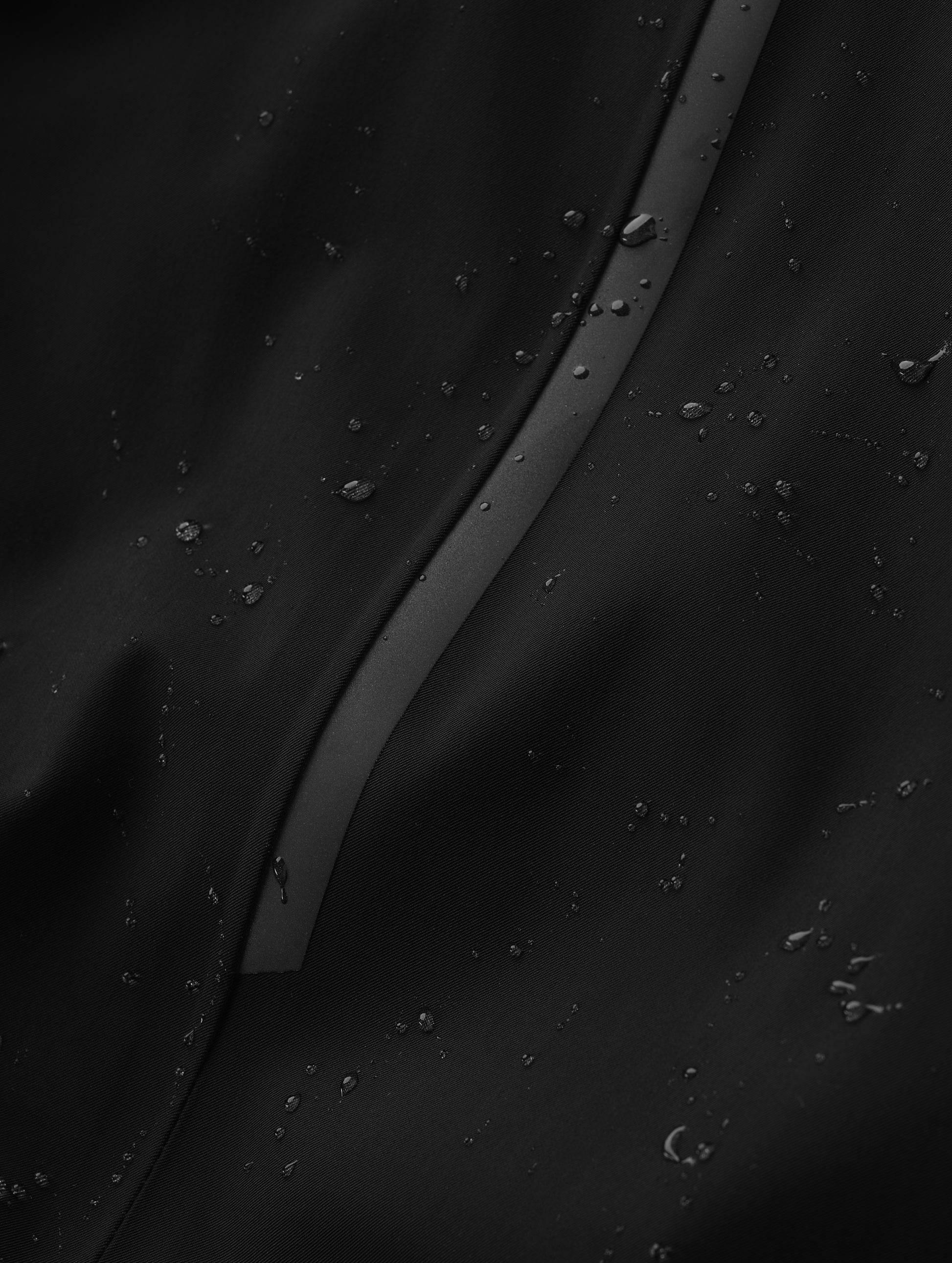 Closeup detailed view of the waterproof stretch fabric construction on the Maxwell Insulated Trench in Onyx Black from AETHER Apparel.