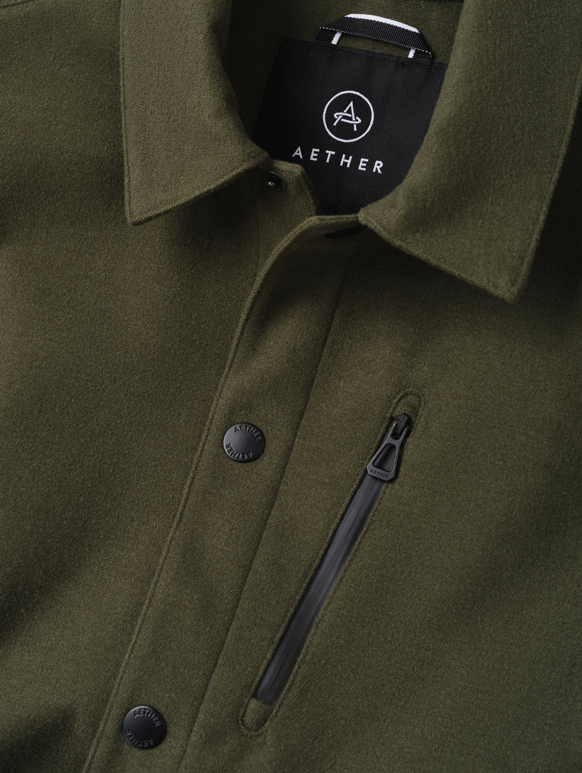 Closeup detailed view of the center-front snap closure and zipper-secured chest pocket on the Milton Chore Jacket in Forest Green from AETHER Apparel. 