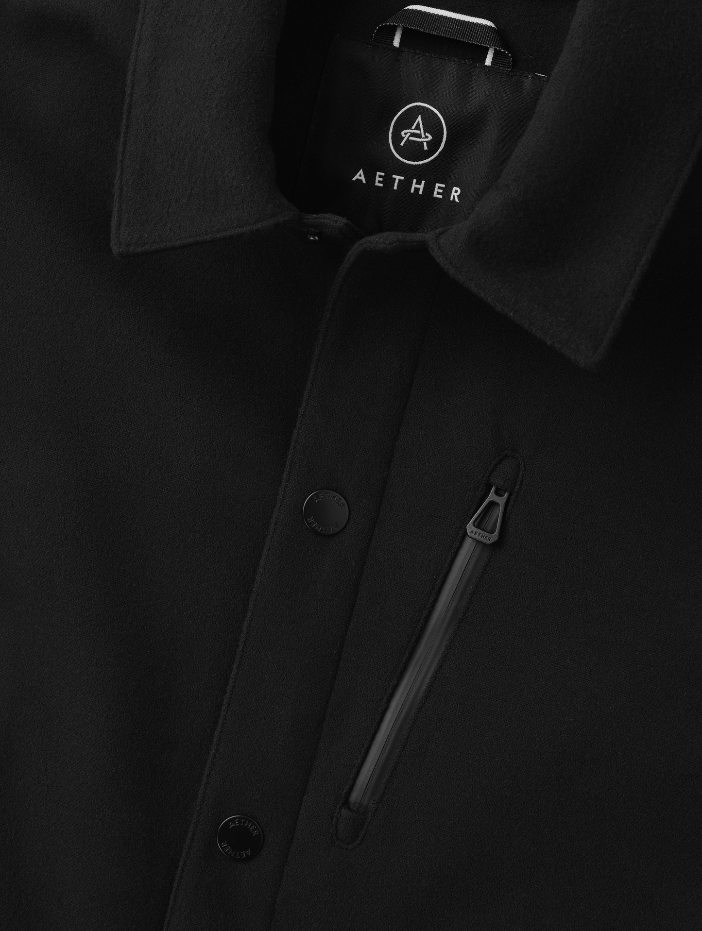 Closeup detailed view of the center-front snap closure and zipper-secured chest pocket on the Milton Chore Jacket in Onyx Black from AETHER Apparel. 