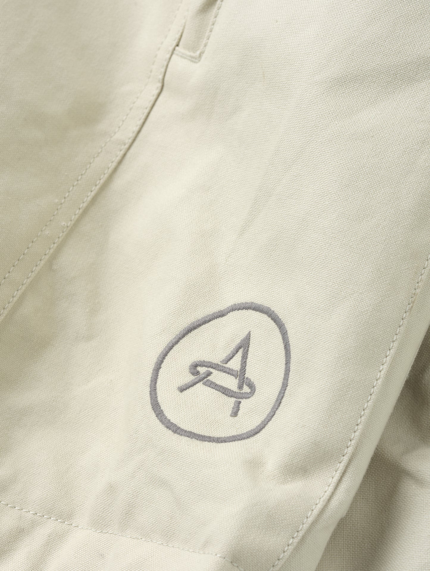 Closeup detailed view of the embroidered AETHER logo on the Mojave Motorcycle Jacket 2.0 in Bone from AETHER Apparel.