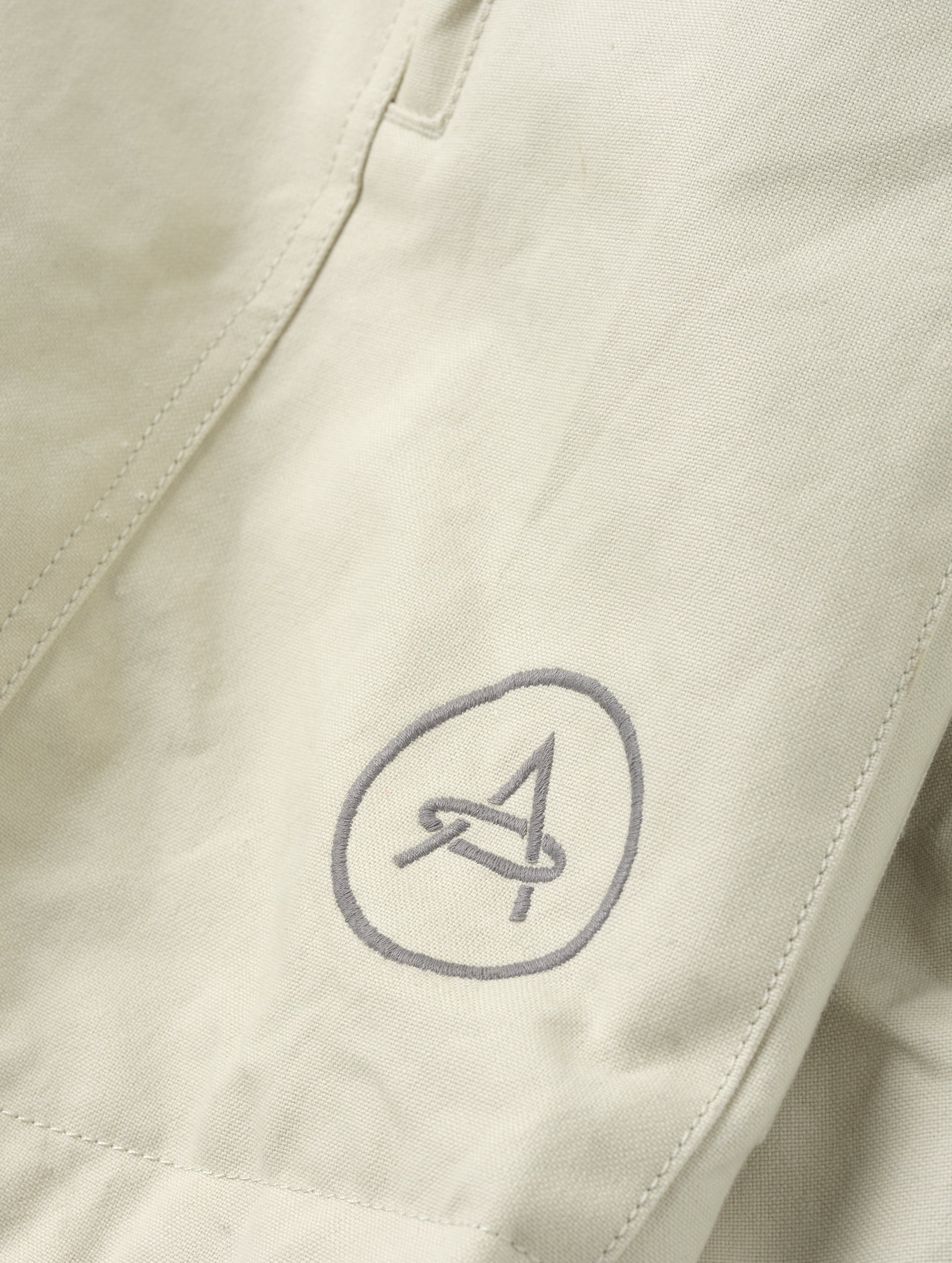 Closeup detailed view of the embroidered AETHER logo on the Mojave Motorcycle Jacket 2.0 in Bone from AETHER Apparel.