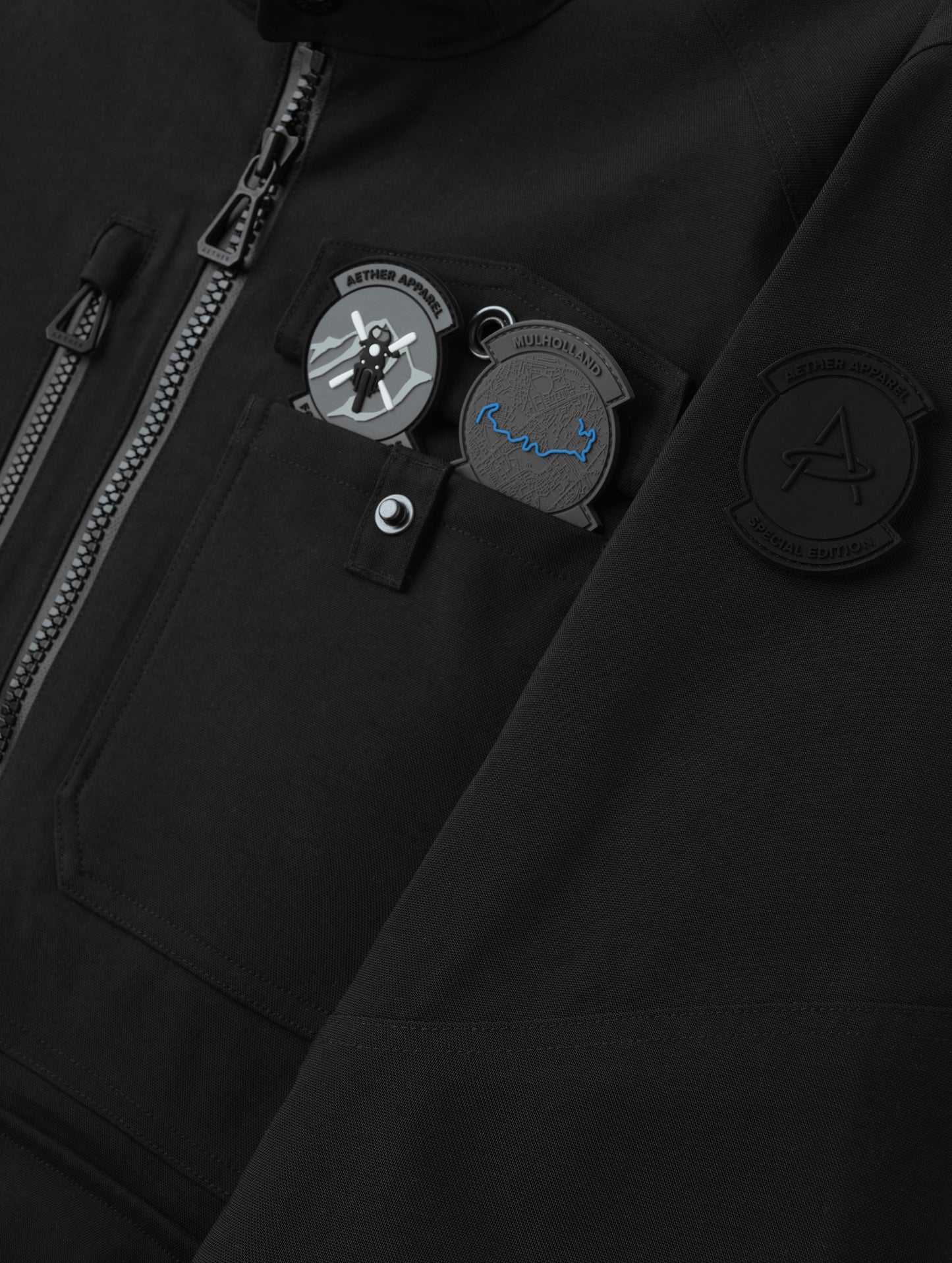 Closeup detailed view of the center-front zipper, chest pocket, and trio of included PVC patches that come with the Mulholland Motorcycle Jacket Special Edition in Onyx Black from AETHER Apparel.