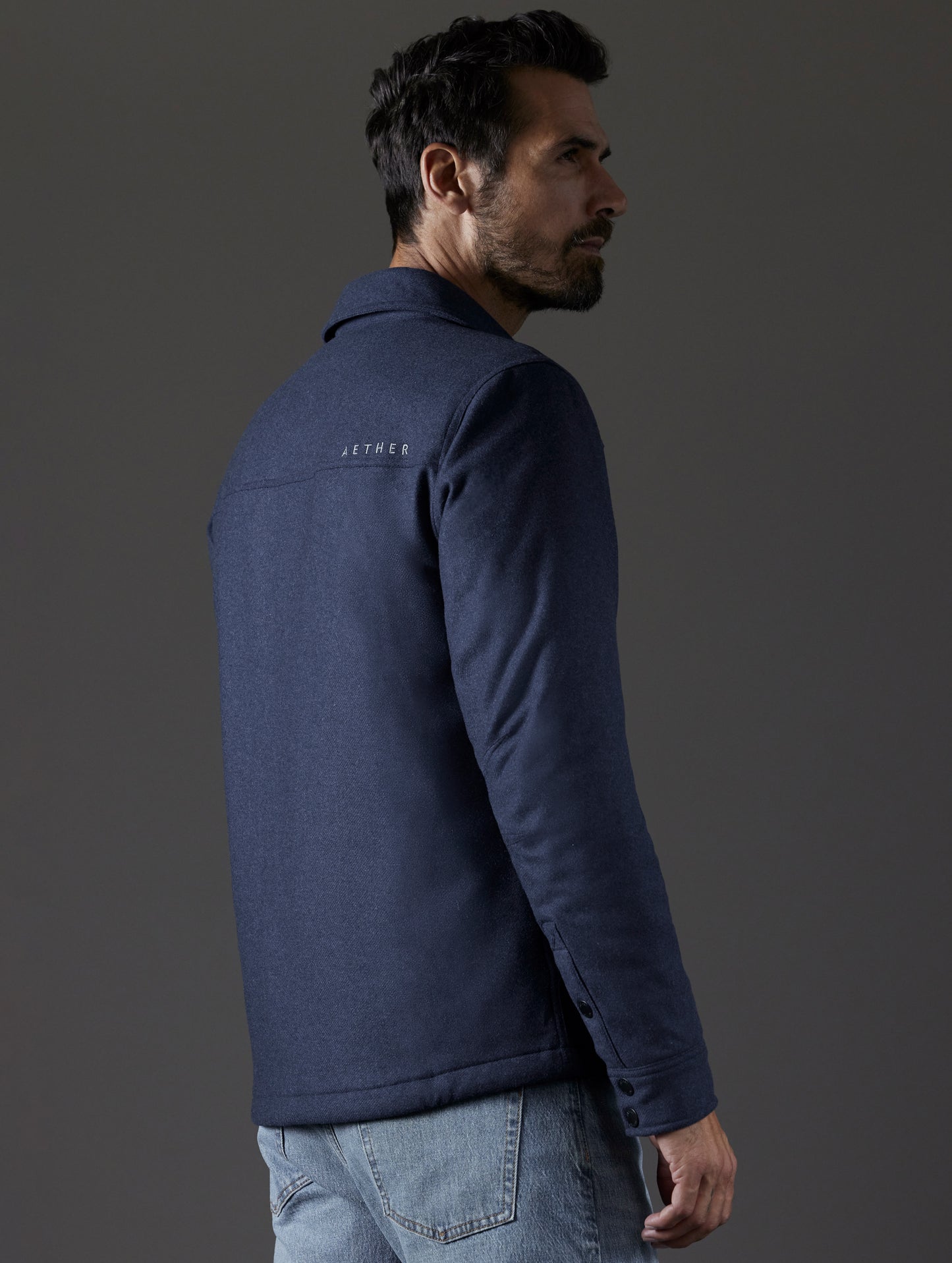 Rear 3/4 body view of man wearing Nova Insulated Button-Down in Total Eclipse Heather dark blue from AETHER Apparel.