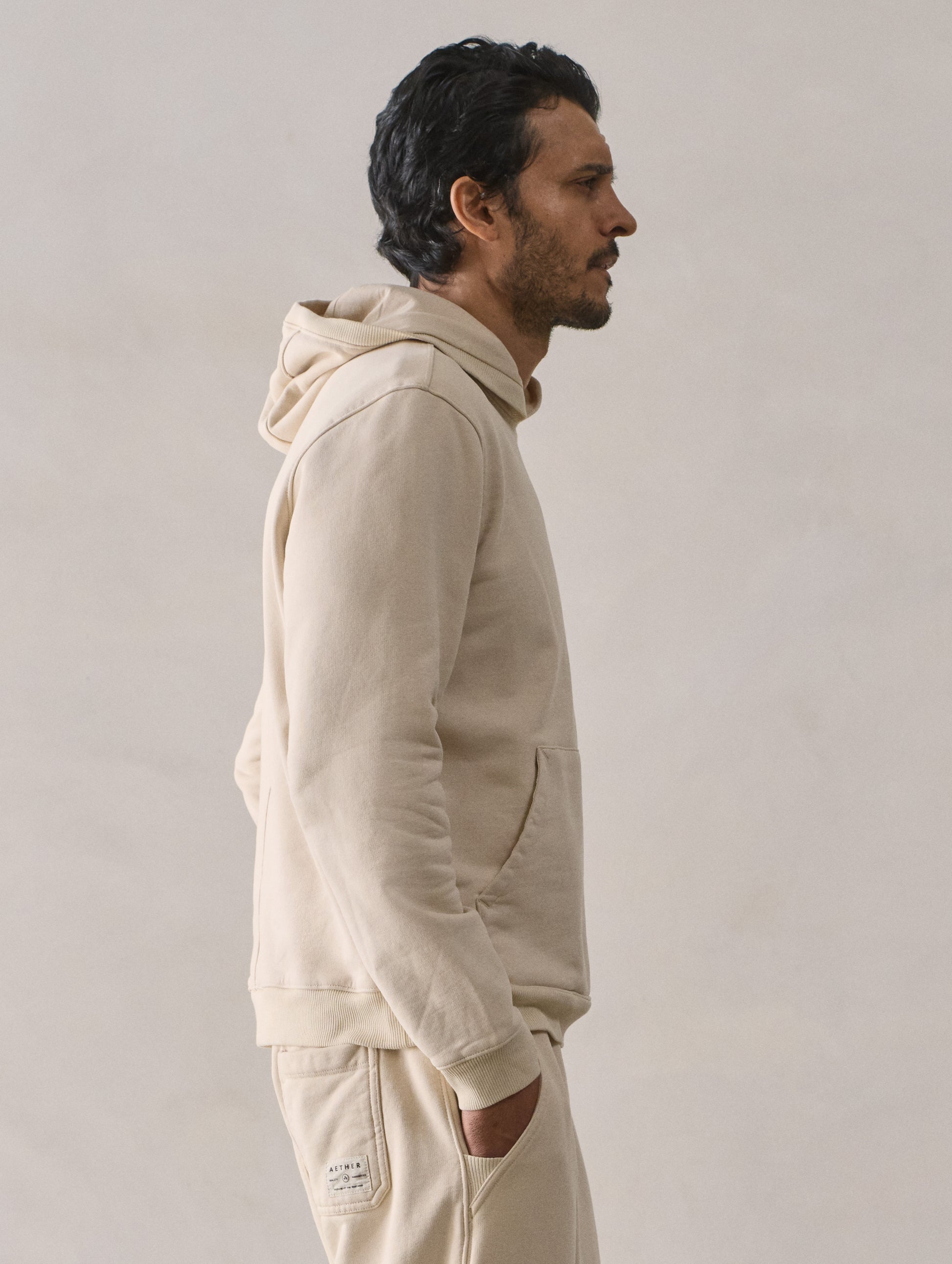 Right side upper body profile view of man wearing Osa Pullover Hoodie in Bone white from AETHER Apparel.