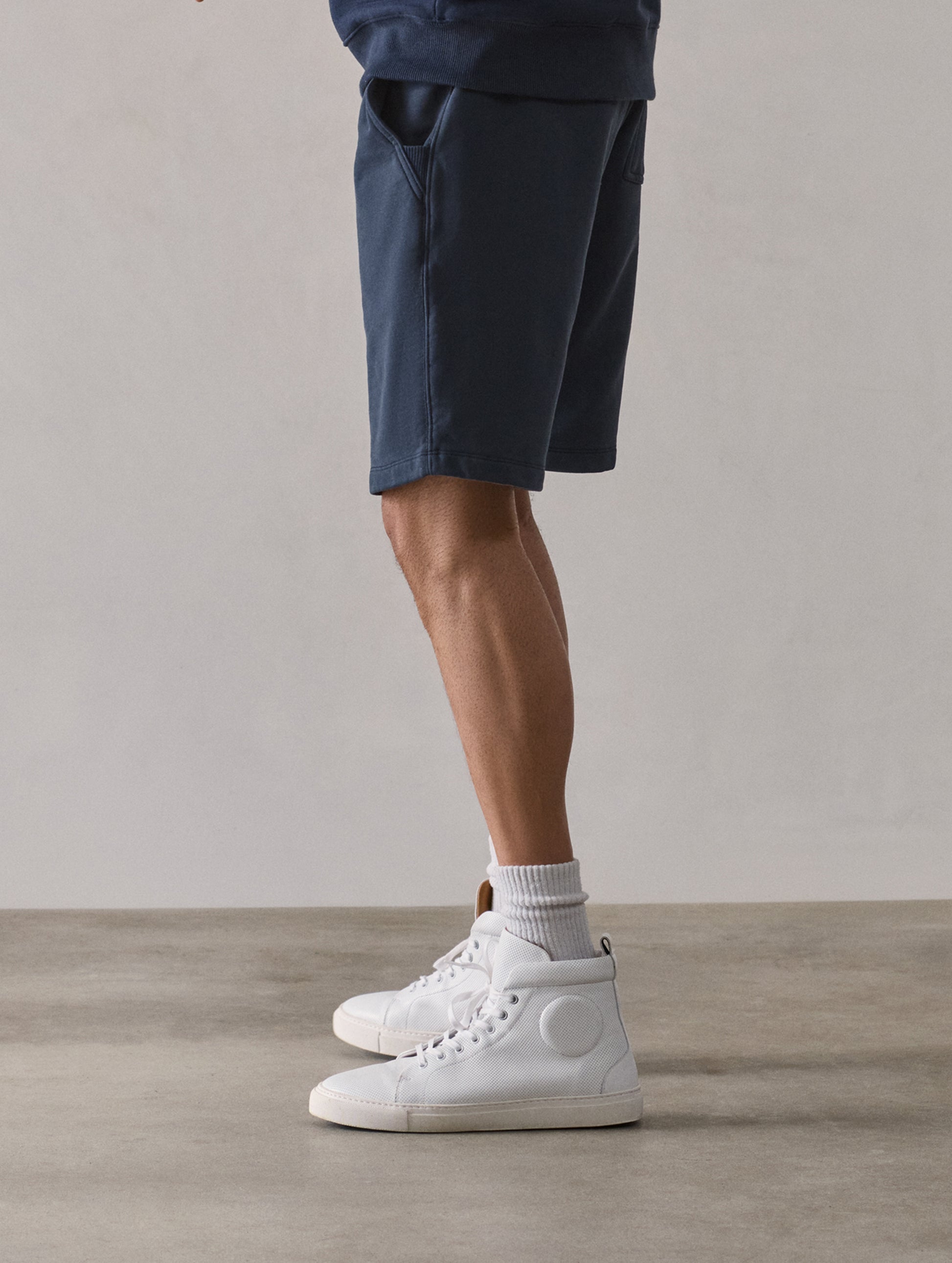 Left side profile lower-body view of man wearing Osa Sweatshort in Total Eclipse dark blue from AETHER Apparel.