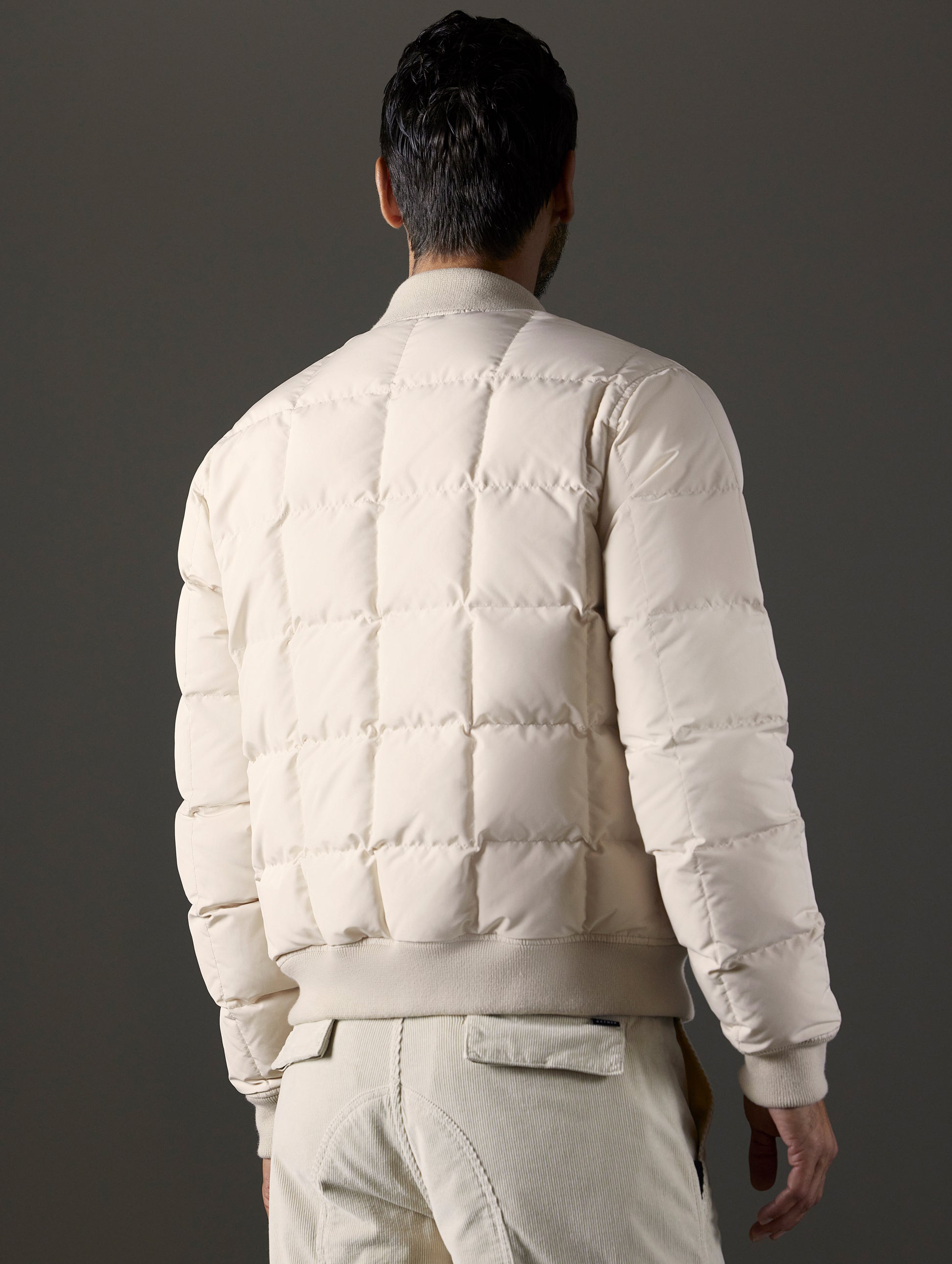 Rear 3/4 body view of man wearing Pacer Jacket in Bone white from AETHER Apparel.