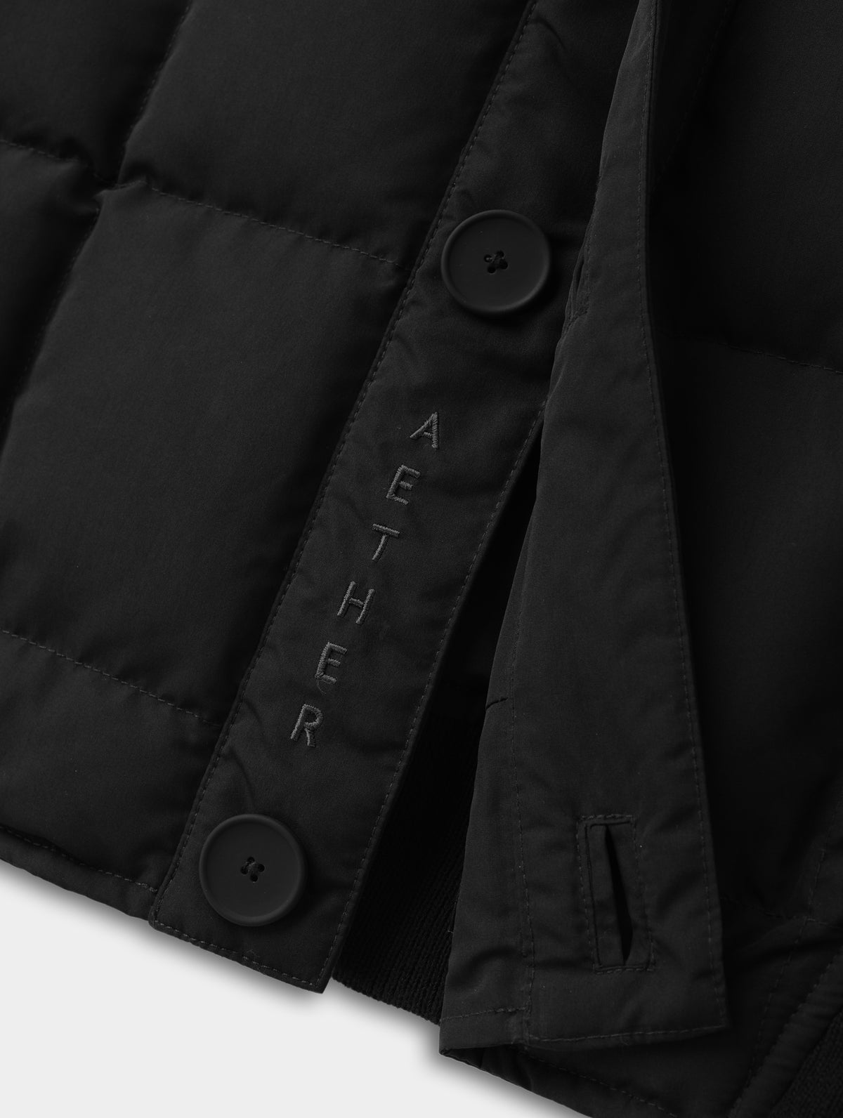 Closeup detailed view of the embroidered AETHER wordmark on the Pacer Jacket in Onyx Black from AETHER Apparel.