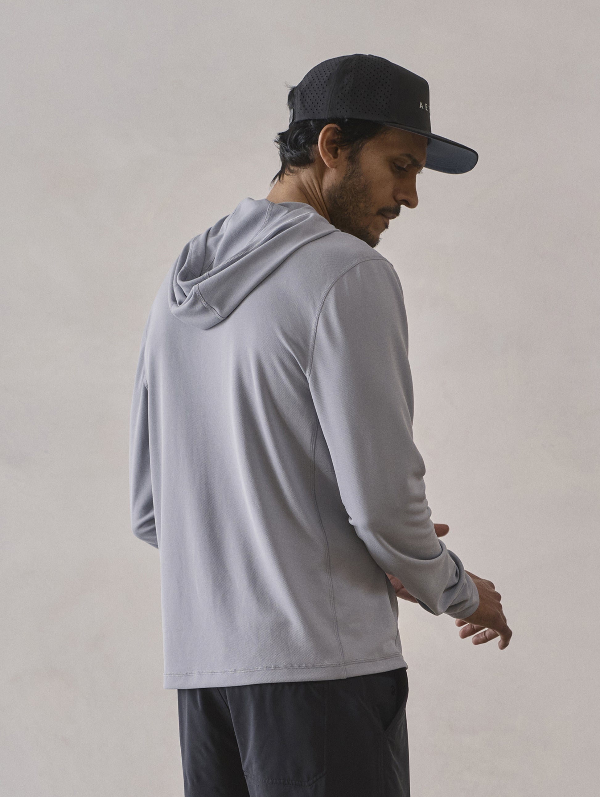 Rear 3/4 upper-body view of man wearing Pacific Hooded Sun Shirt in Sky Grey from AETHER Apparel.