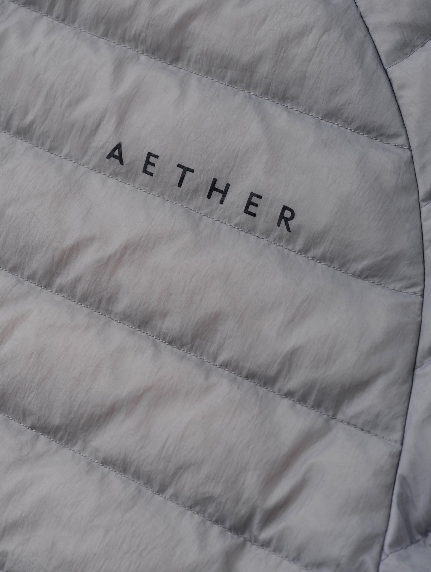 Closeup detailed view of the AETHER wordmark on the Prospect Packable Down Jacket in Sky Grey from AETHER Apparel.