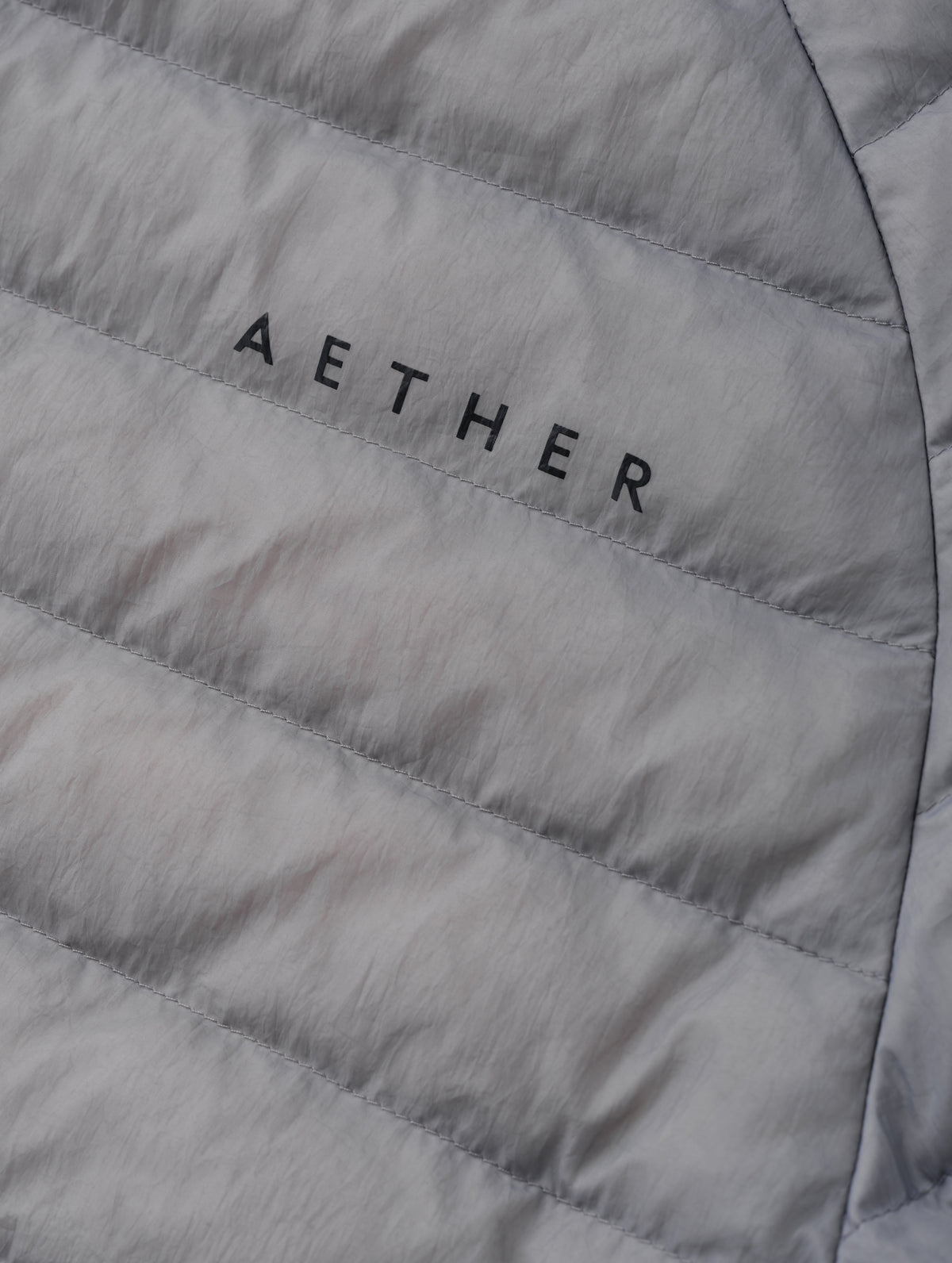 Closeup detailed view of the AETHER wordmark on the Prospect Packable Down Jacket in Sky Grey from AETHER Apparel.