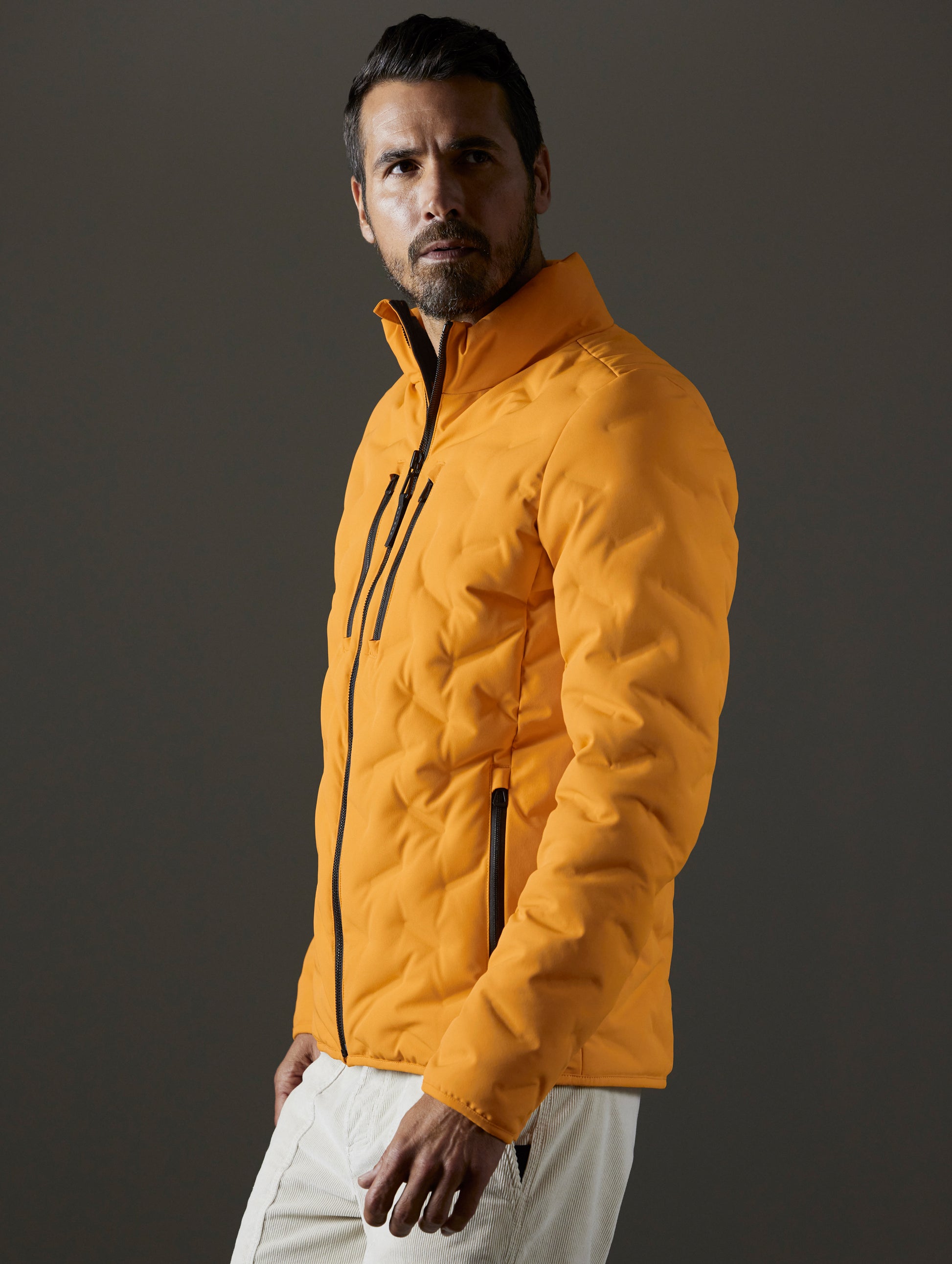 Front 3/4 body view of man wearing Rex Down Jacket in Midas Orange from AETHER Apparel.