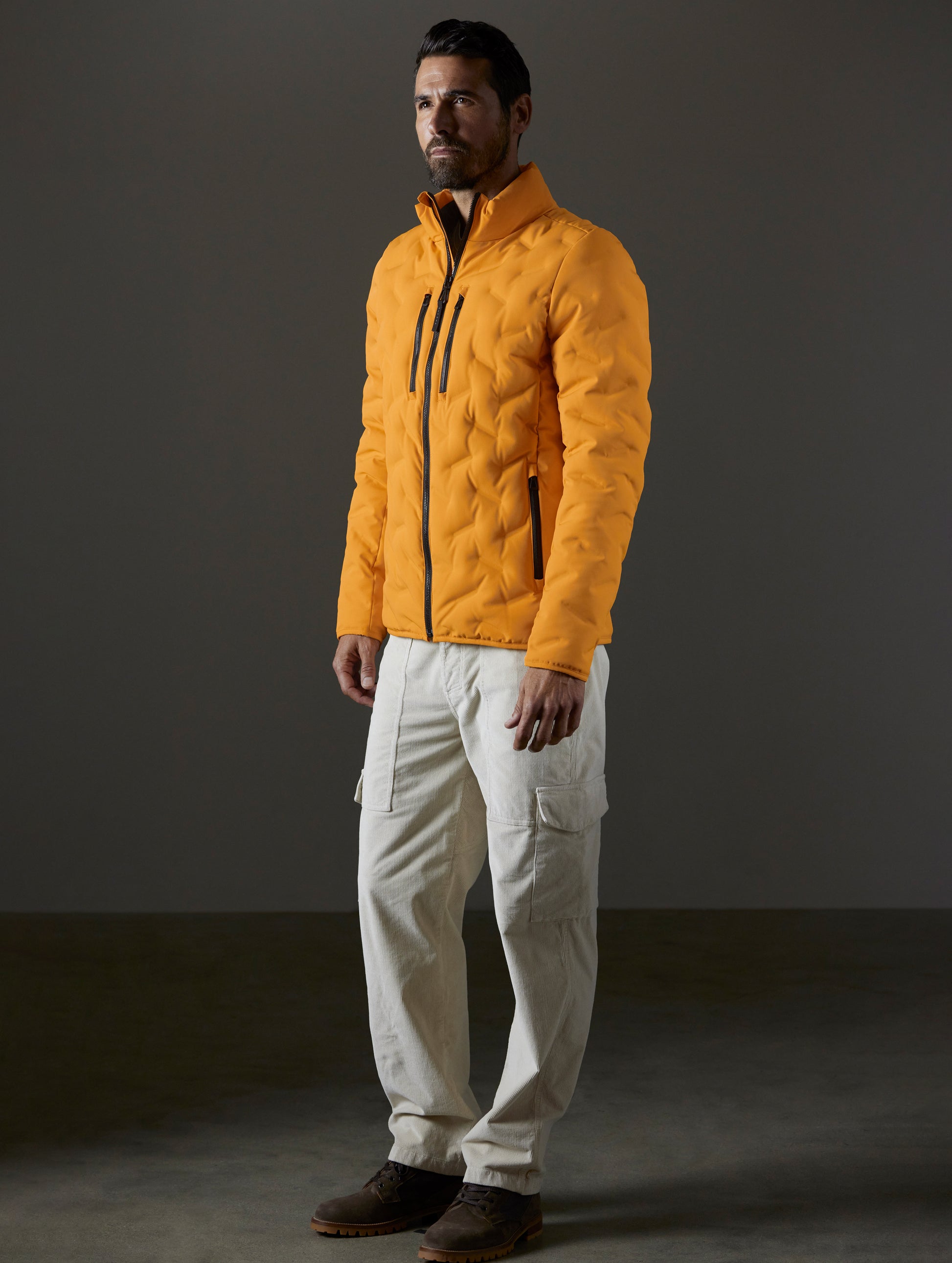 Front 3/4 full-body view of man wearing Rex Down Jacket in Midas Orange from AETHER Apparel.