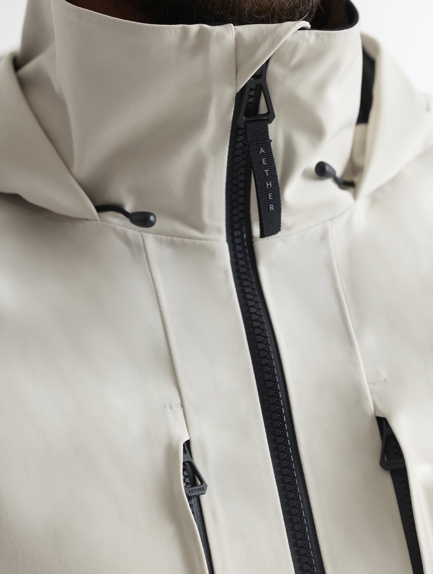 Closeup detailed view of the main center-front zipper, vertical zipper-secured chest pockets, and collar on the Ridge Snow-Shell Jacket in Bone from AETHER Apparel.