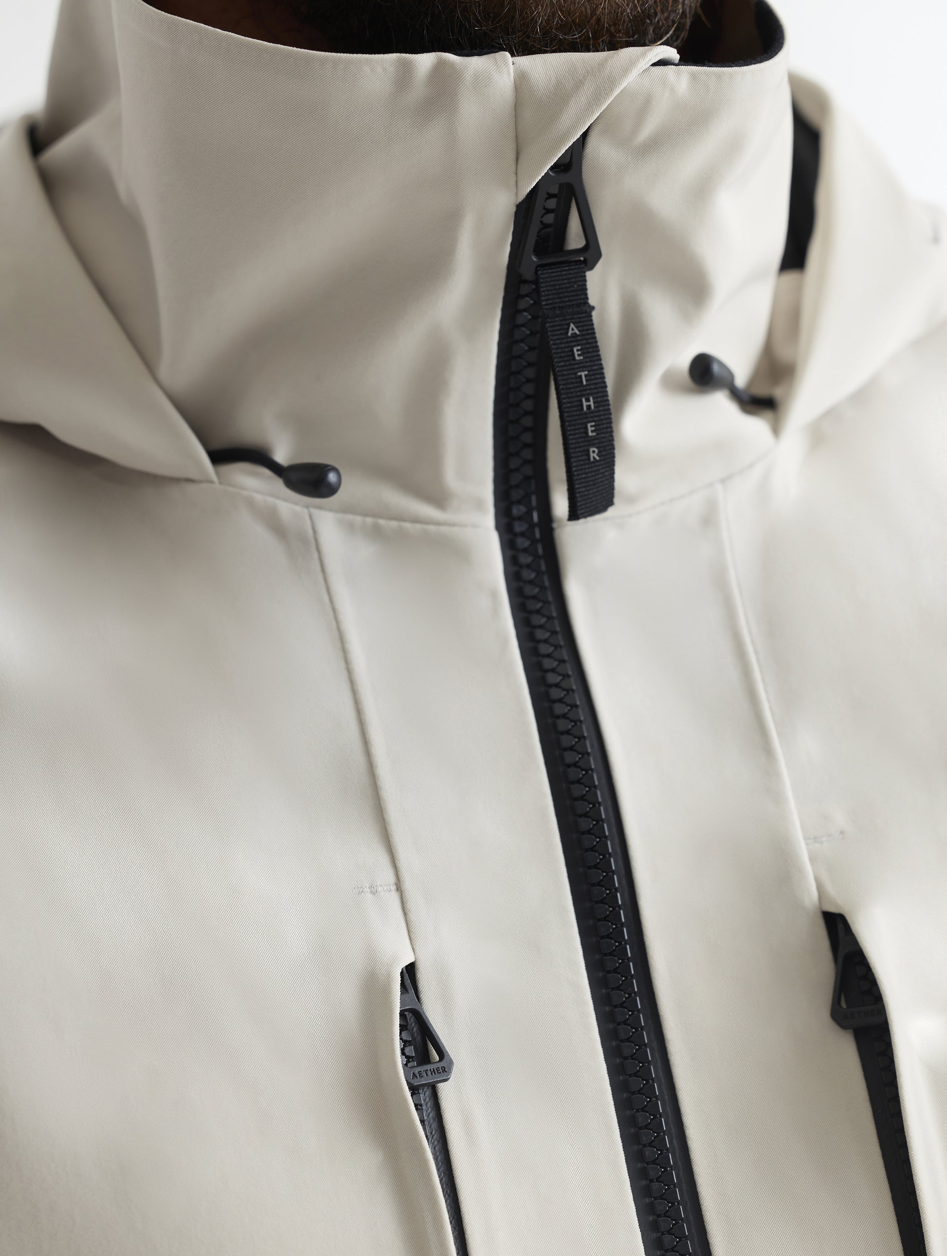 Closeup detailed view of the main center-front zipper, vertical zipper-secured chest pockets, and collar on the Ridge Snow-Shell Jacket in Bone from AETHER Apparel.