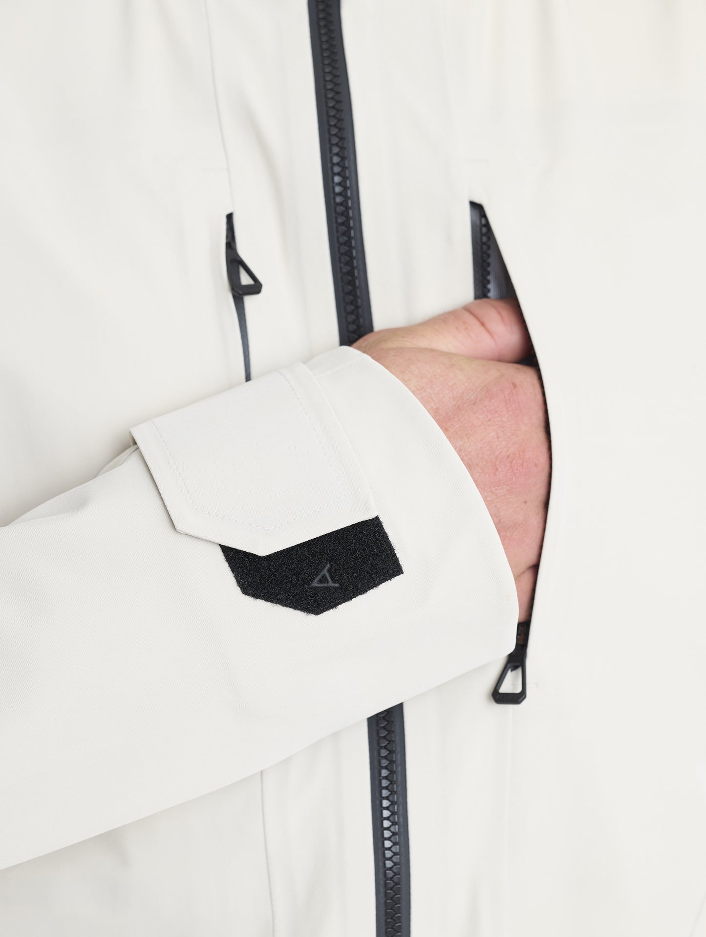 Closeup detailed view of man placing hands into the zipper-secured vertical chest pockets on the Ridge Snow-Shell Jacket in Bone from AETHER Apparel.