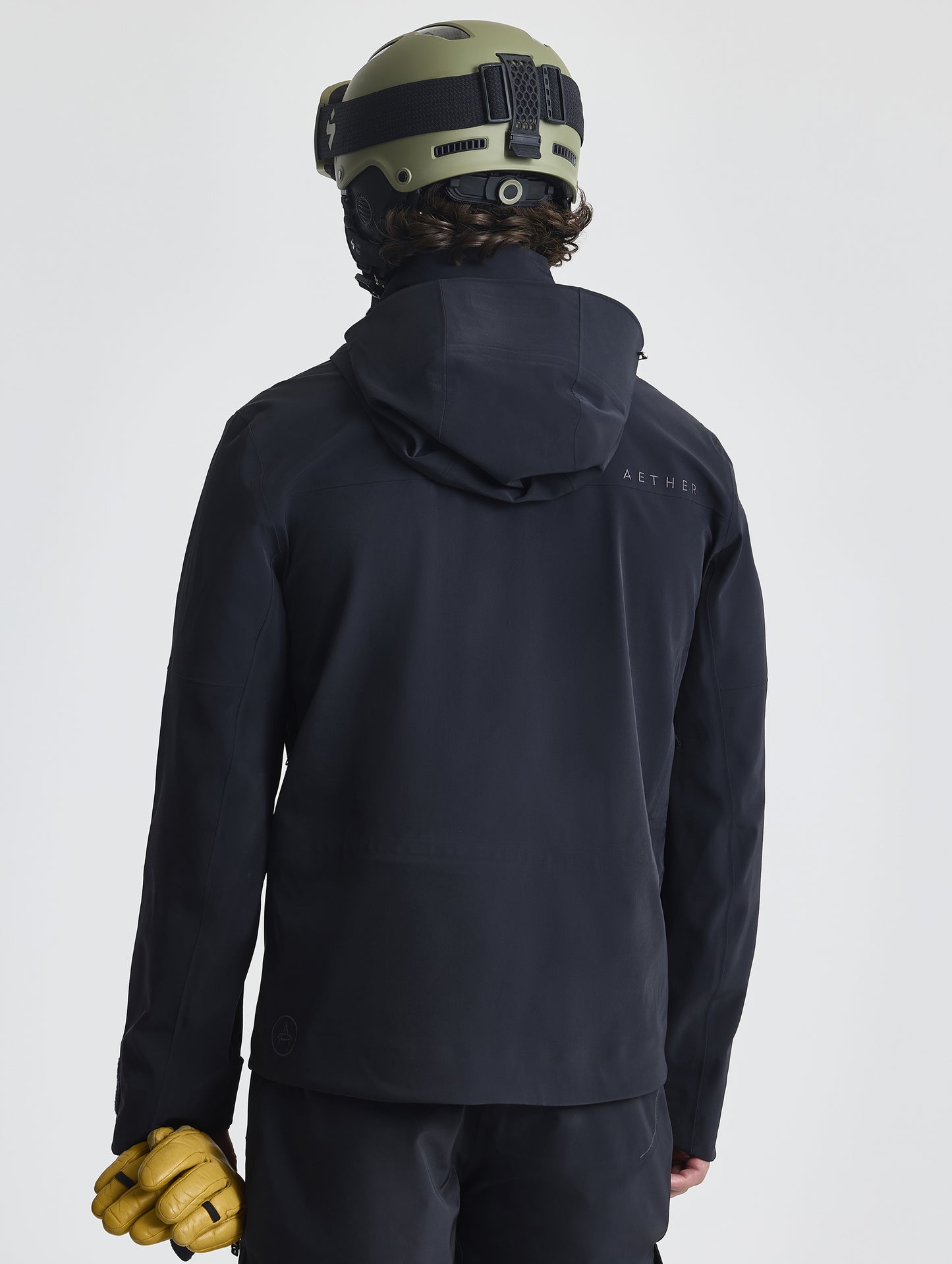 Rear angled upper-body view of man wearing the Ridge Snow-Shell Jacket in Onyx Black from AETHER Apparel.