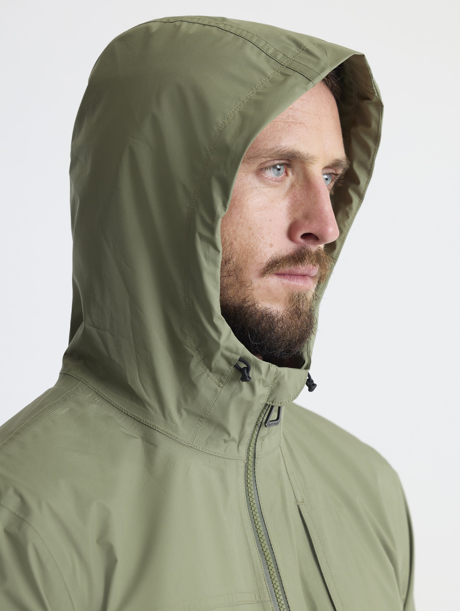 Man wearing hood of Storm All-Weather Jacket in Fern Green from AETHER Apparel.