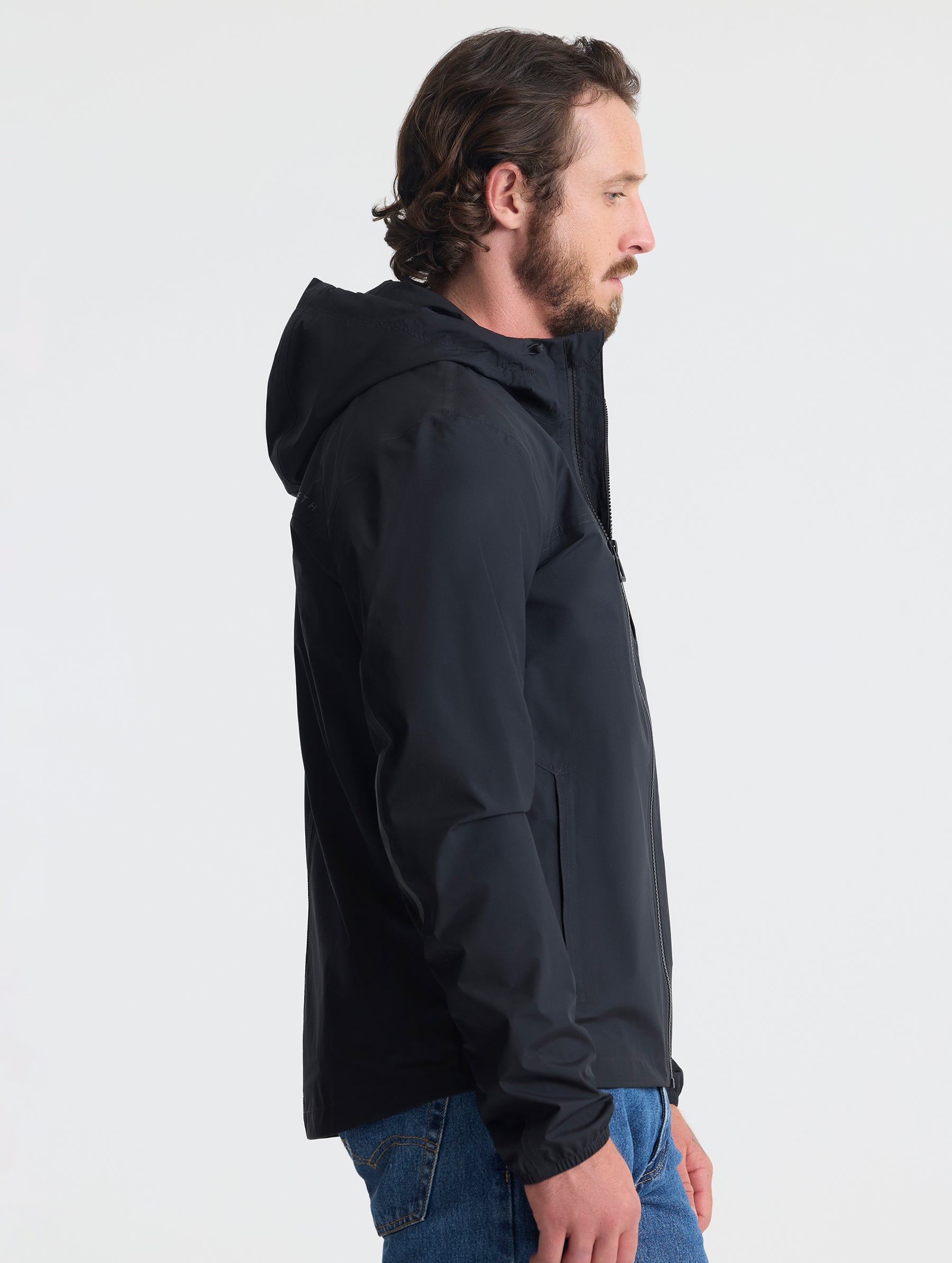 Right profile view of man wearing Storm All-Weather Jacket in Onyx Black from AETHER Apparel.