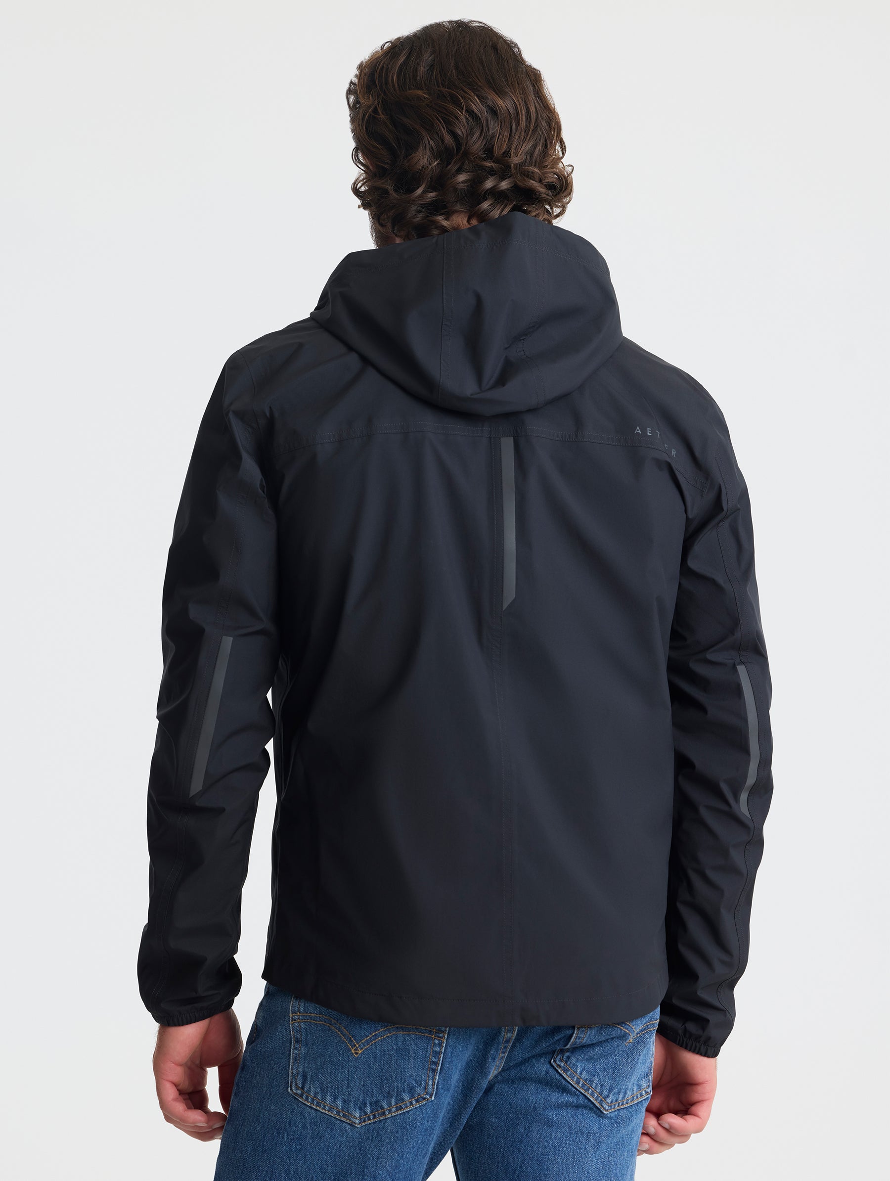 Rear view of man wearing Storm All-Weather Jacket in Onyx Black from AETHER Apparel.