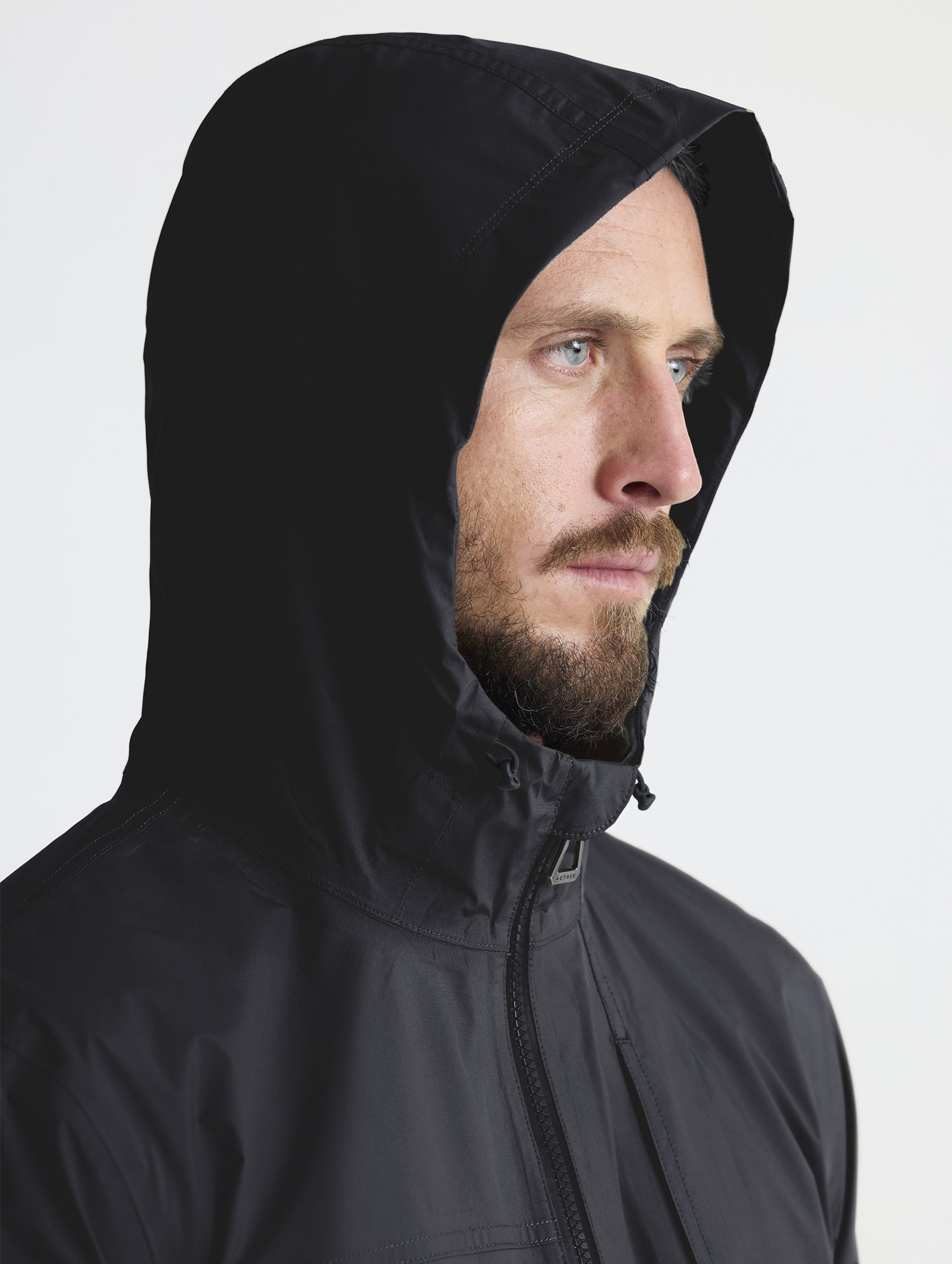 Man wearing hood of Storm All-Weather Jacket in Onyx Black from AETHER Apparel.