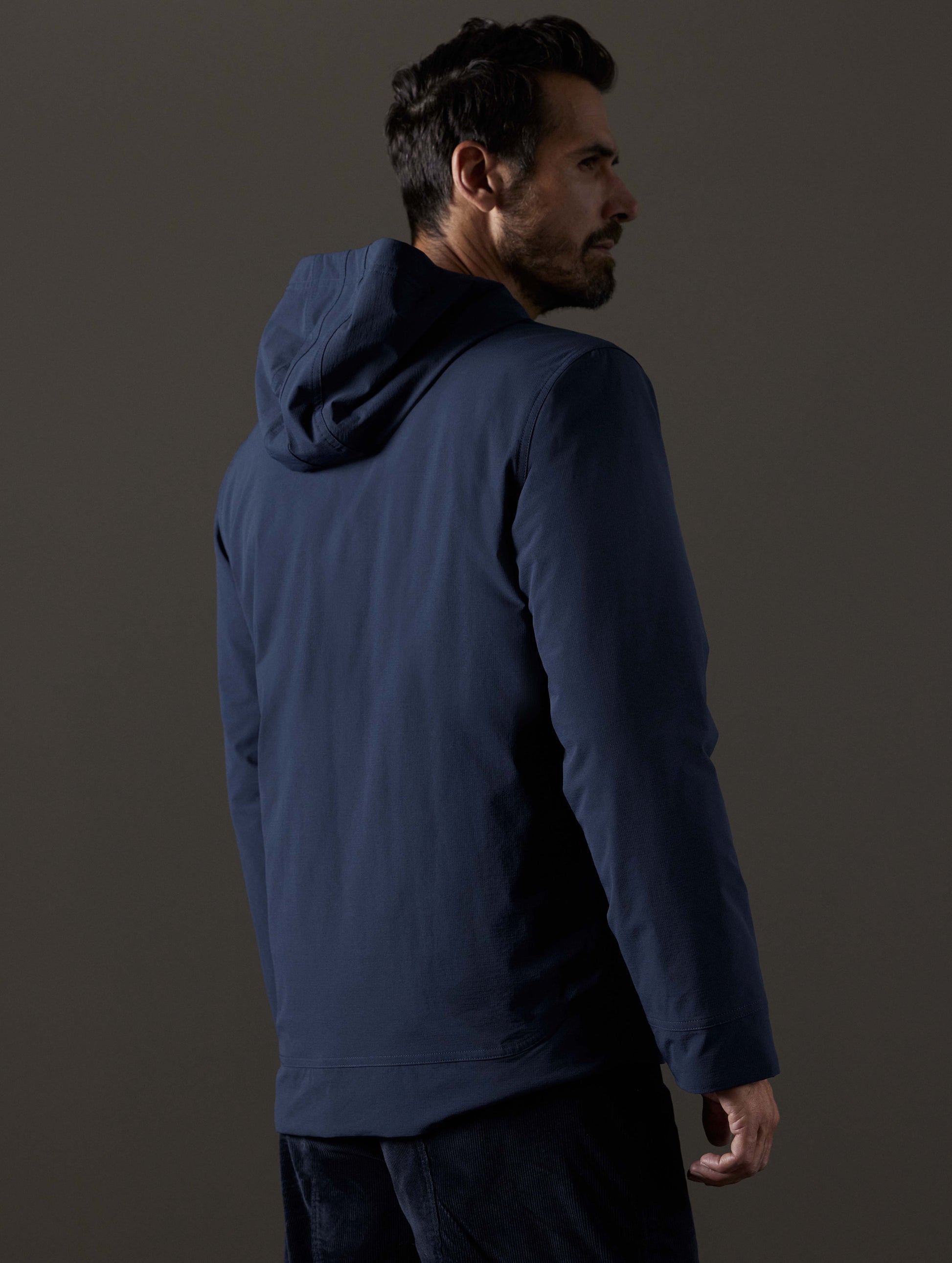 Rear 3/4 body view of man wearing Stornaway Insulated Hoodie in Total Eclipse dark blue from AETHER Apparel.