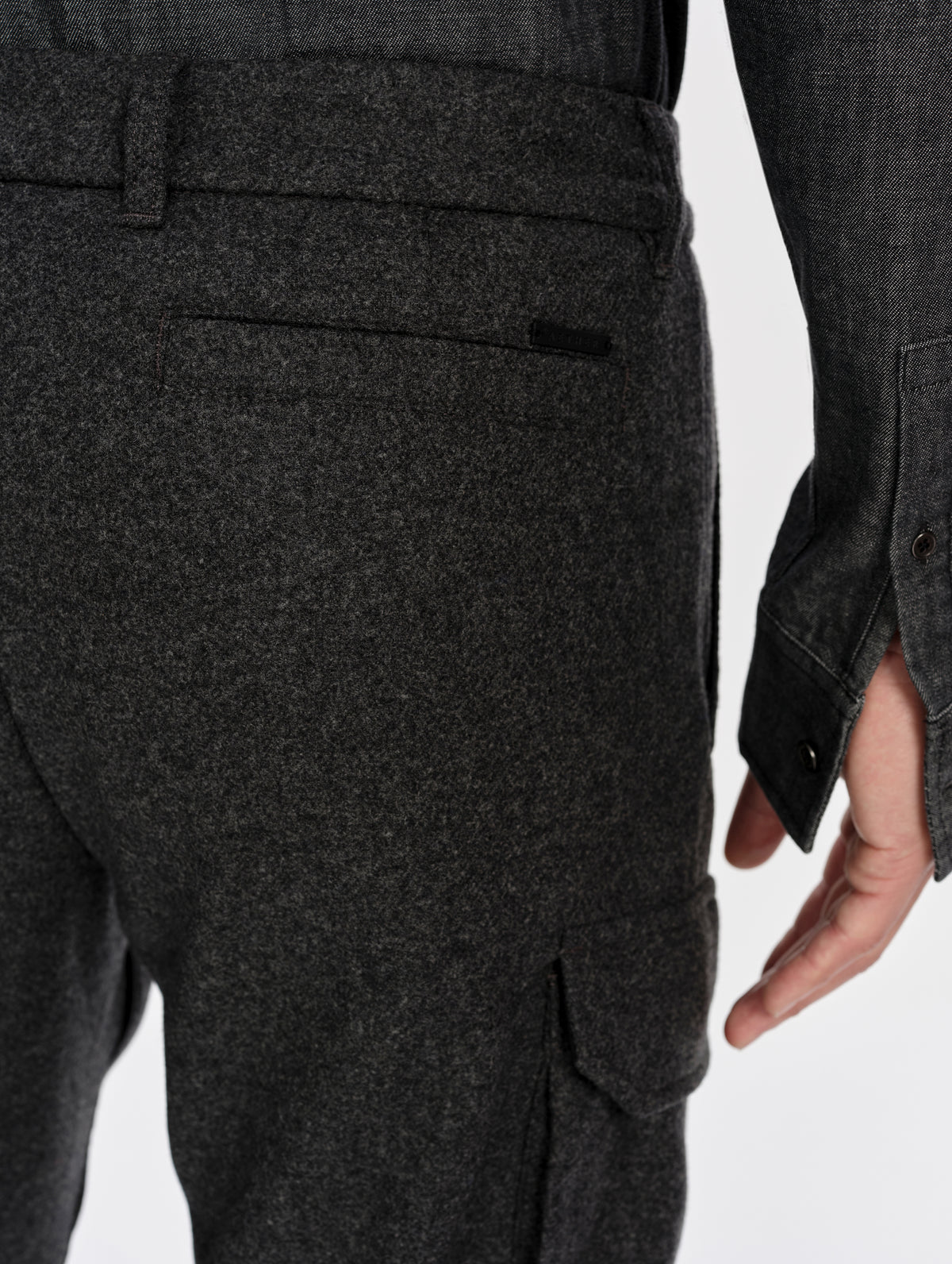 Closeup detailed view of the back welt pockets and the metal AETHER logo plate on the Strata Wool Pant in Charcoal Heather from AETHER Apparel.