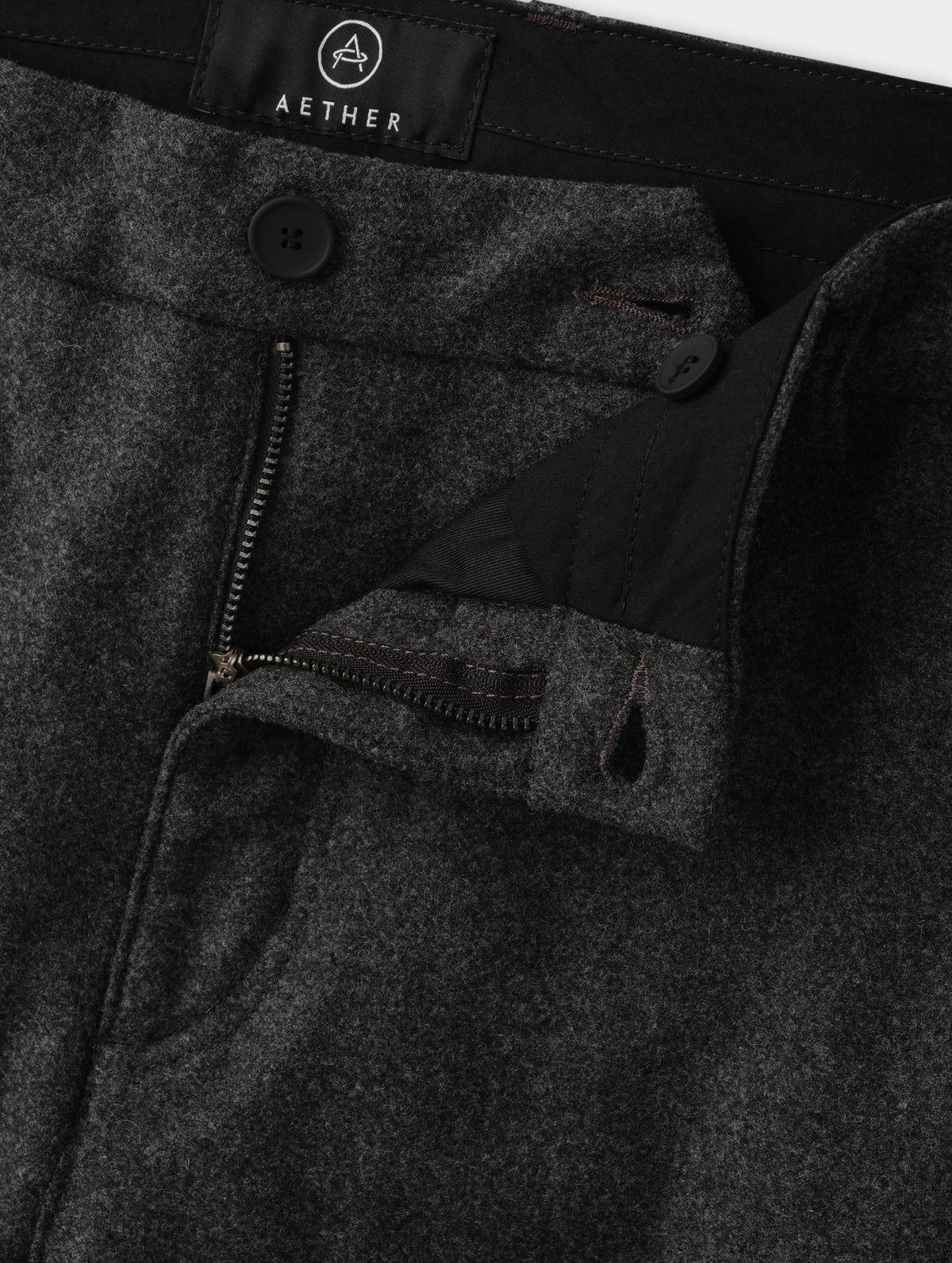 Closeup detailed view of the zippered fly, rubberized button, and waistband extension with button closure on the Strata Wool Pant in Charcoal Heather from AETHER Apparel.