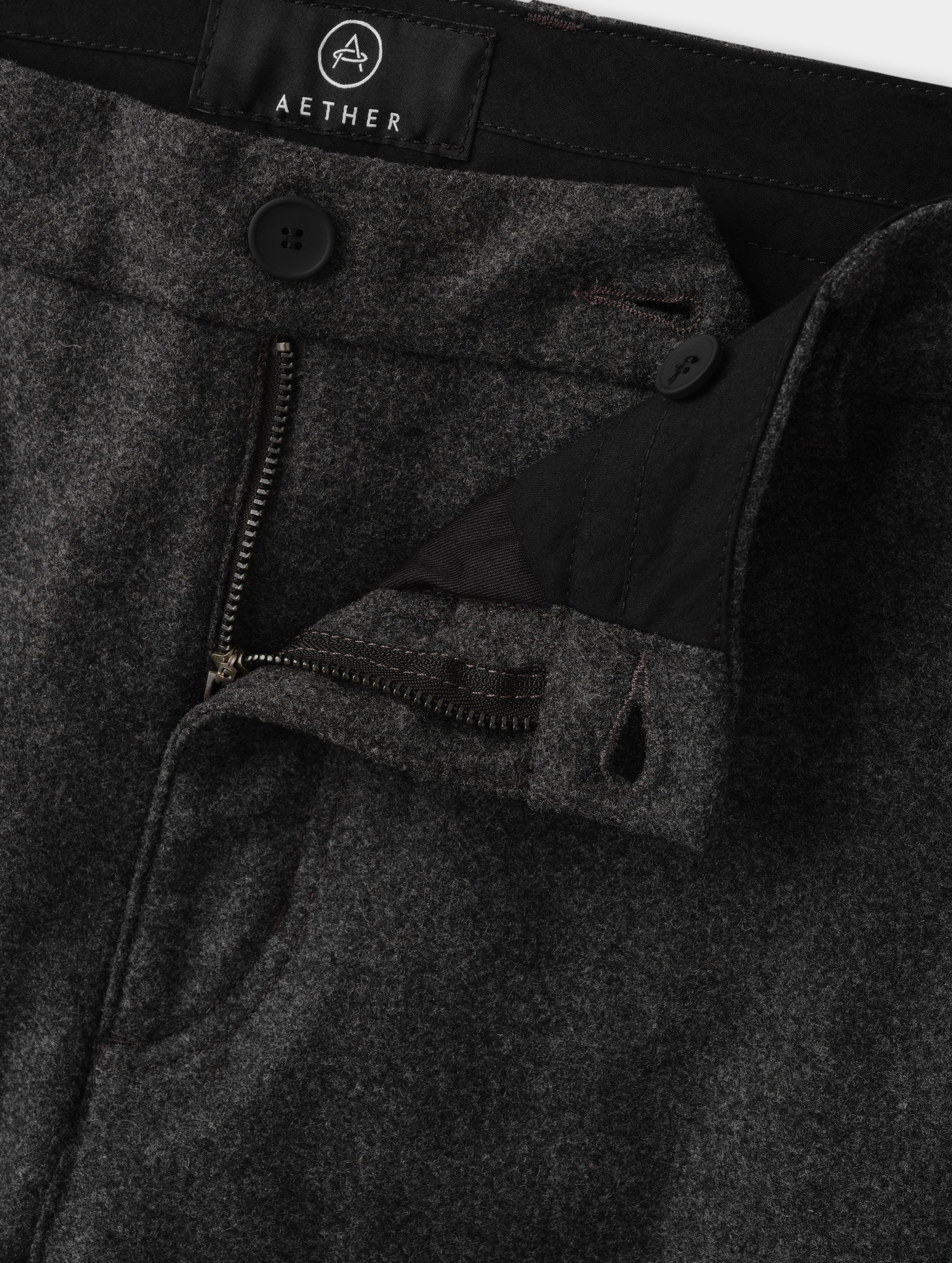 Closeup detailed view of the zippered fly, rubberized button, and waistband extension with button closure on the Strata Wool Pant in Charcoal Heather from AETHER Apparel.