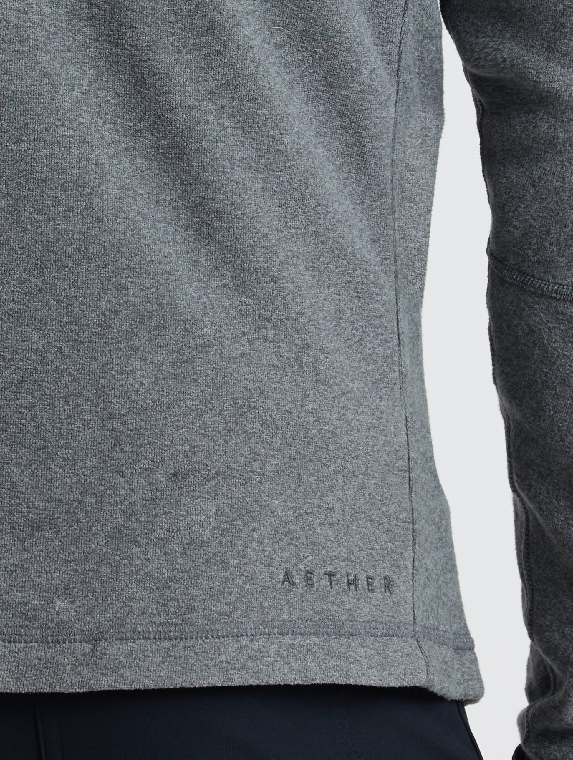 Closeup rear view of AETHER logo above bottom right hem of Sutherlin Full-Zip in Charcoal Grey from AETHER Apparel.