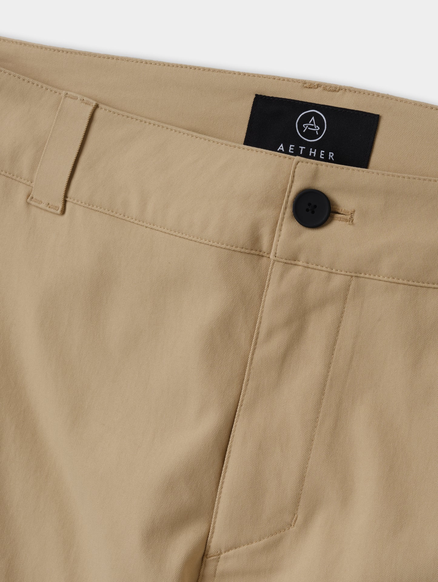 Closeup detailed view of the main center-front button closure and zipper fly on the Walden Tech Pant in Desert Tan from AETHER Apparel. 