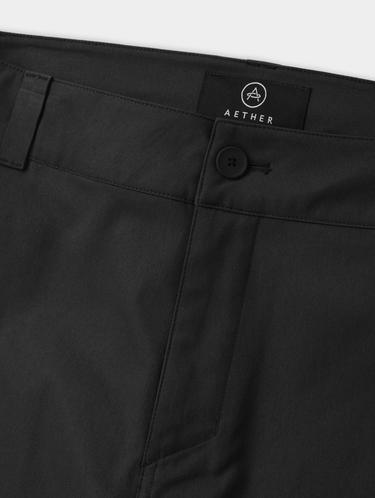Closeup detailed view of the main center-front button closure and zipper fly on the Walden Tech Pant in Onyx Black from AETHER Apparel. 