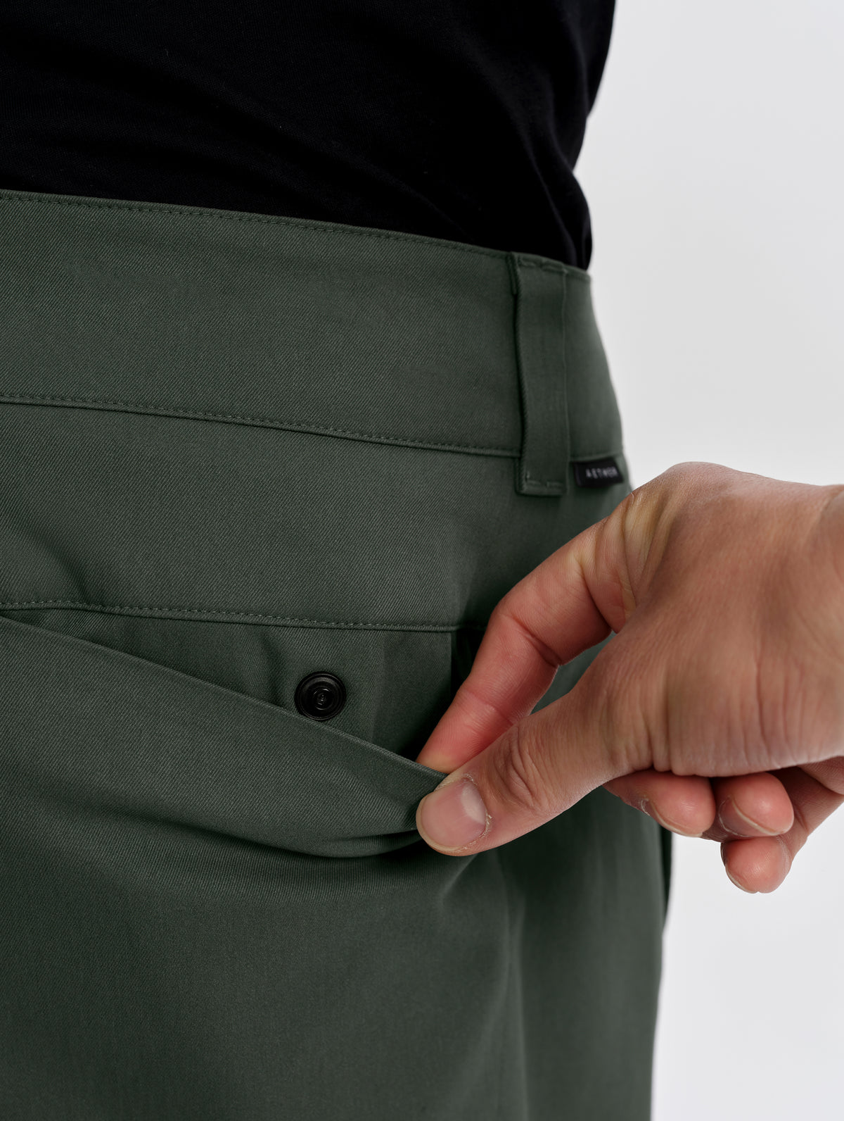 Closeup detailed view of the snap-secured rear pocket on the Walden Tech Pant in Saville Green from AETHER Apparel. 