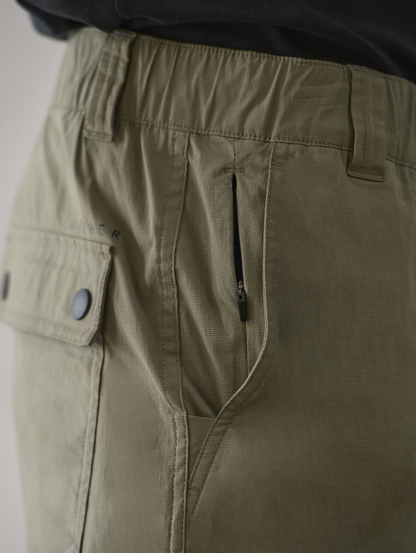 Closeup detailed view of the standard field hand pocket, hidden inner zipper-secured pocket, and flap-snap-secured back patch pockets on the Zermatt Hiking Short in Fern Green from AETHER Apparel.