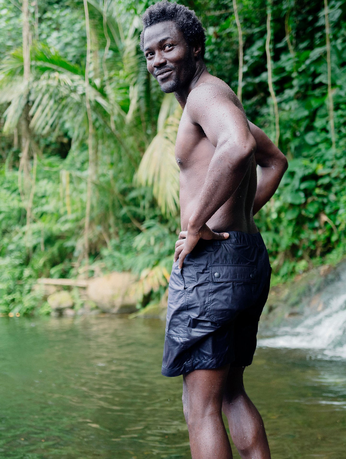 Lifestyle image of man standing in front of swimming hole wearing the Zermatt Hiking Short in Graphite from AETHER Apparel.