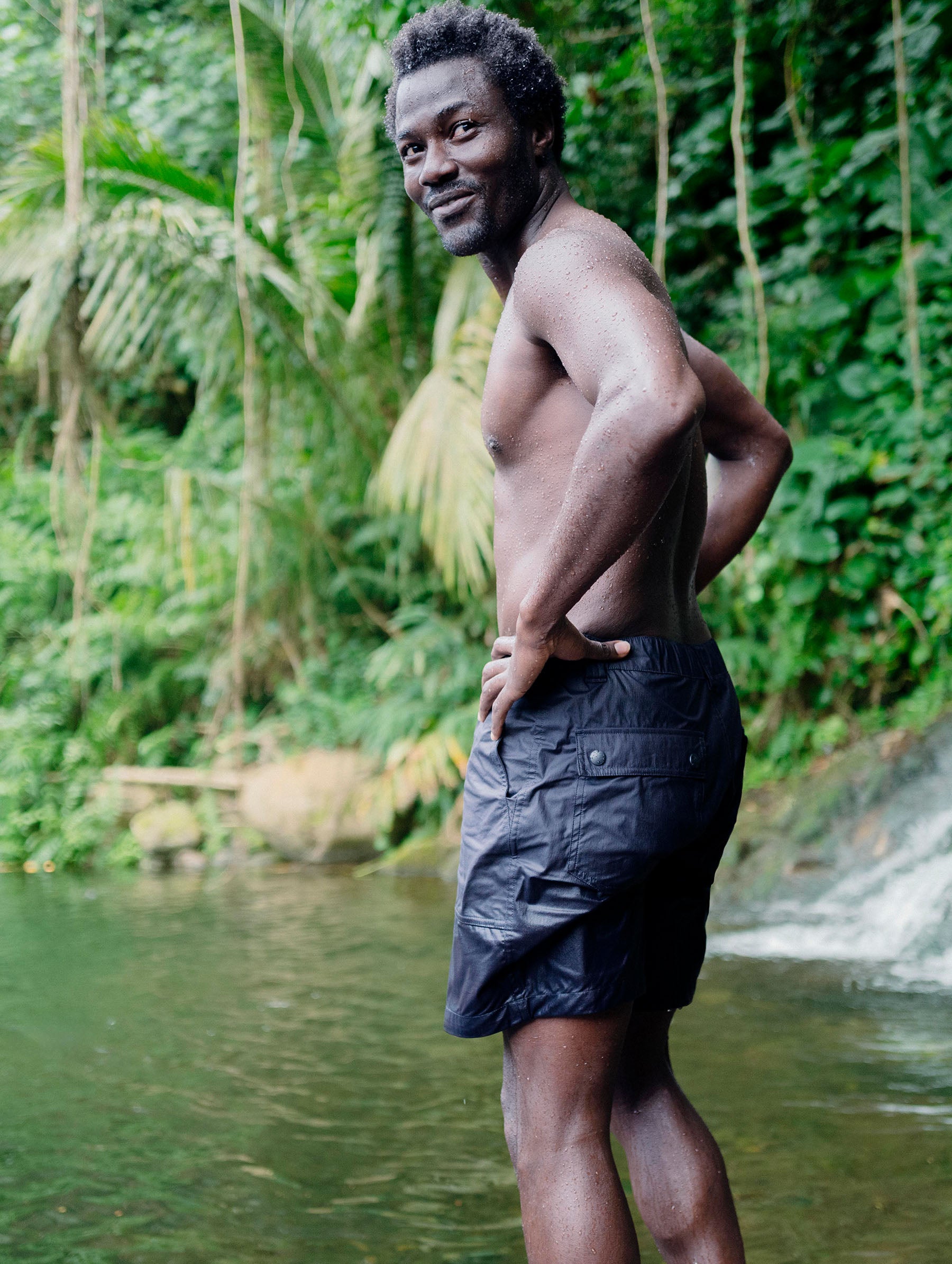Lifestyle image of man standing in front of swimming hole wearing the Zermatt Hiking Short in Graphite from AETHER Apparel.