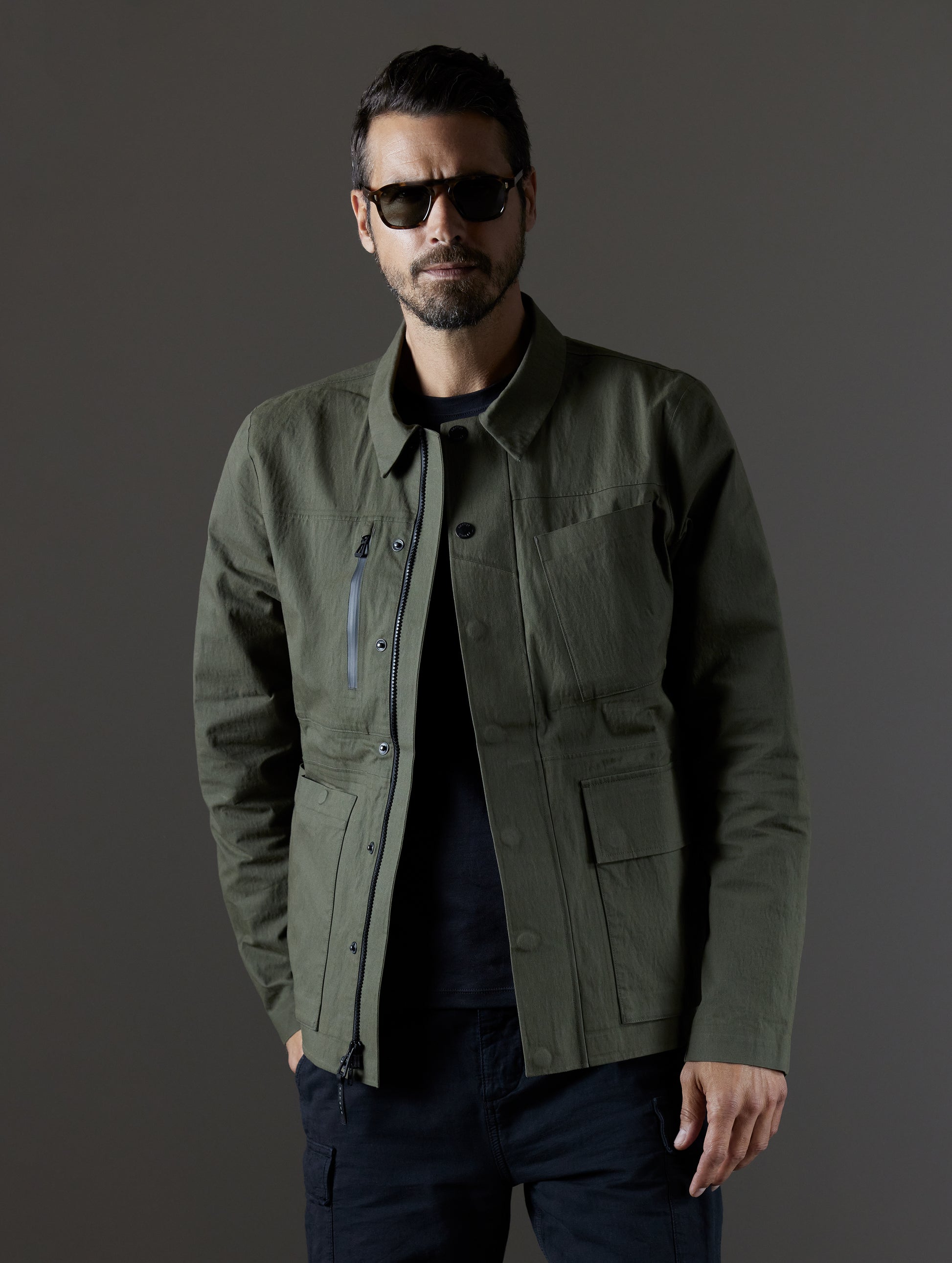 Upper body view of man wearing unzipped green Reporter Jacket from AETHER Apparel.