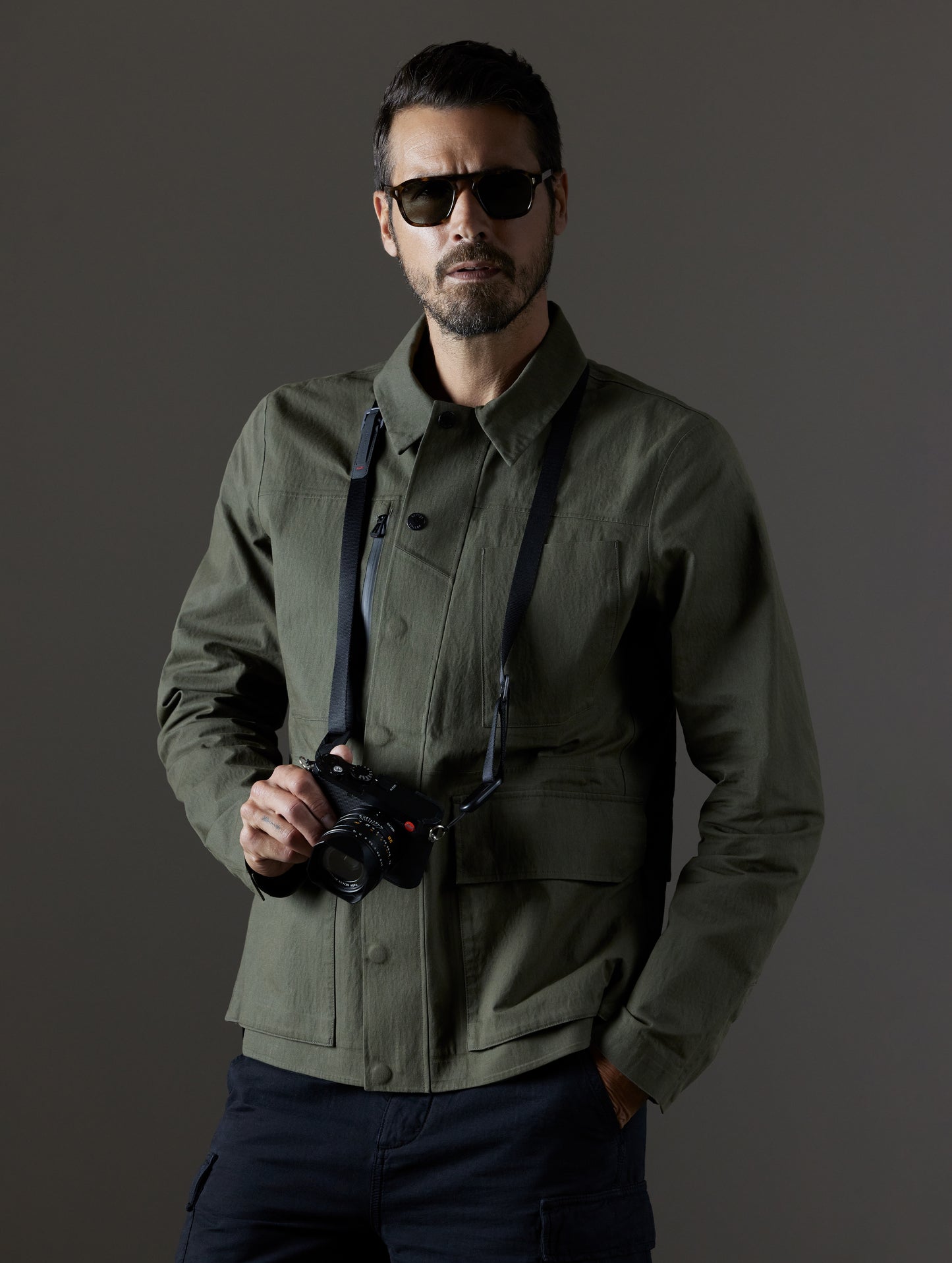 Man wearing camera around neck and green Reporter Jacket from AETHER Apparel.