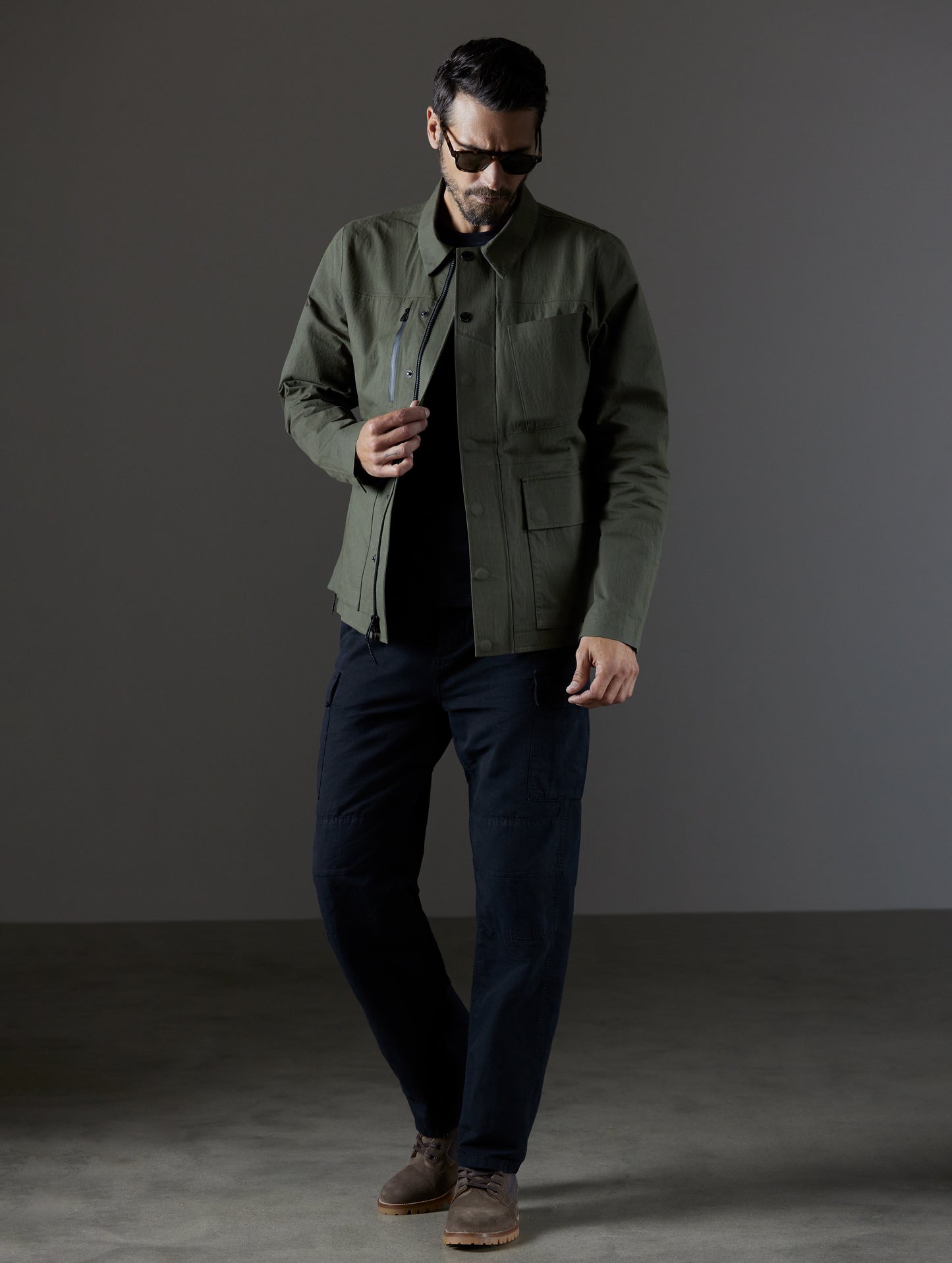 Full-body view of man wearing unzipped green Reporter Jacket from AETHER Apparel.