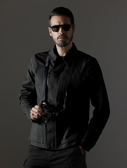 Front upper body view of man wearing buttoned-up AETHER + LEICA Reporter Jacket in Monochrom. 