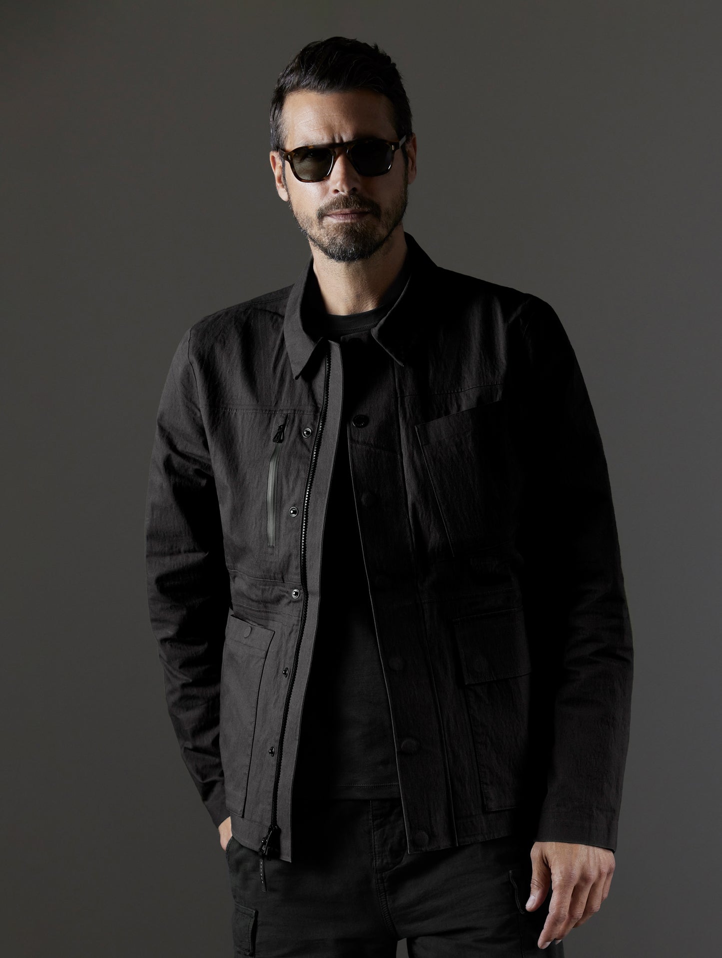 Front upper body view of man wearing unbuttoned AETHER + LEICA Reporter Jacket in Monochrom. 