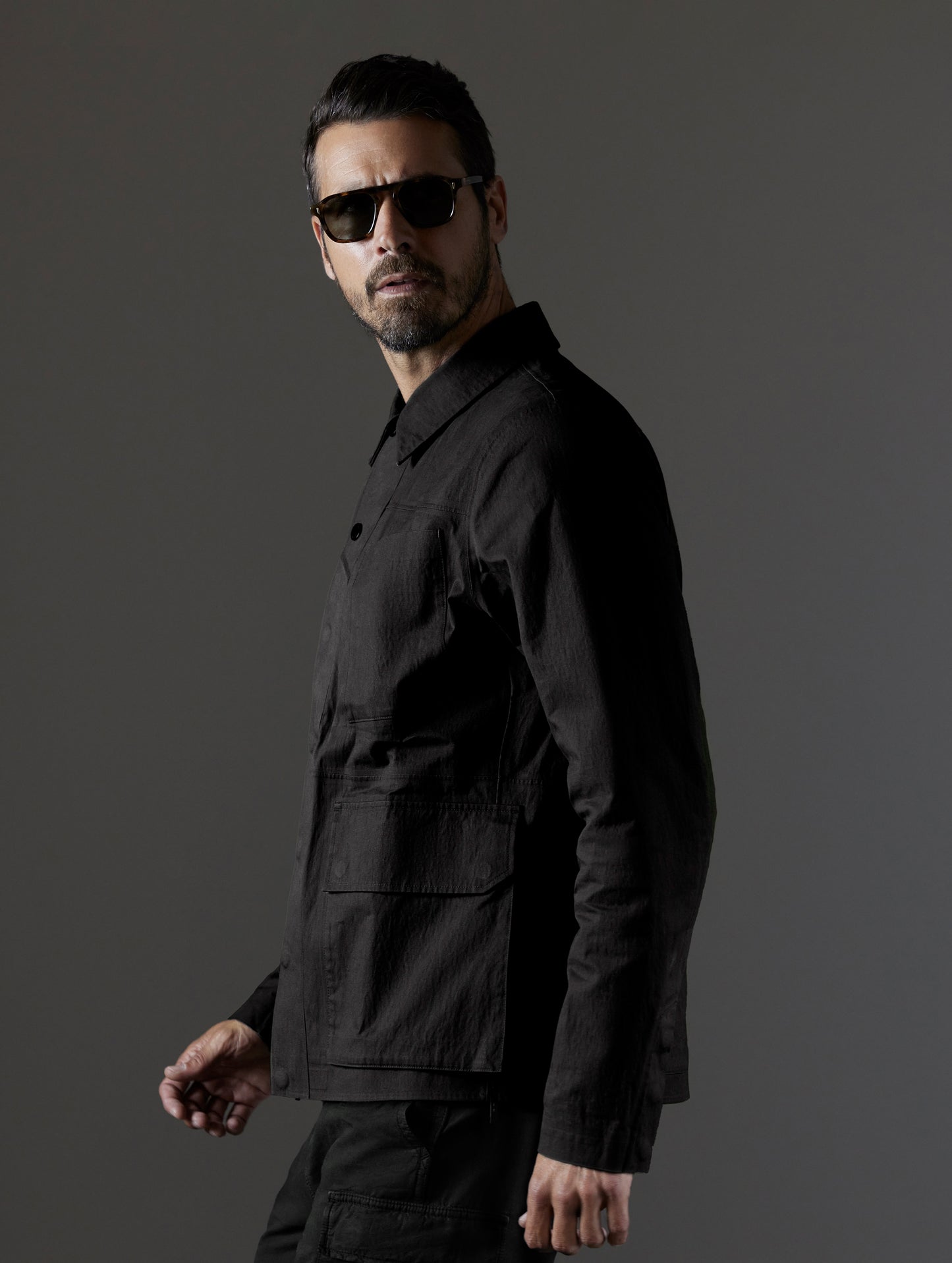 Side profile view of man wearing buttoned-up AETHER + LEICA Reporter Jacket in Monochrom. 