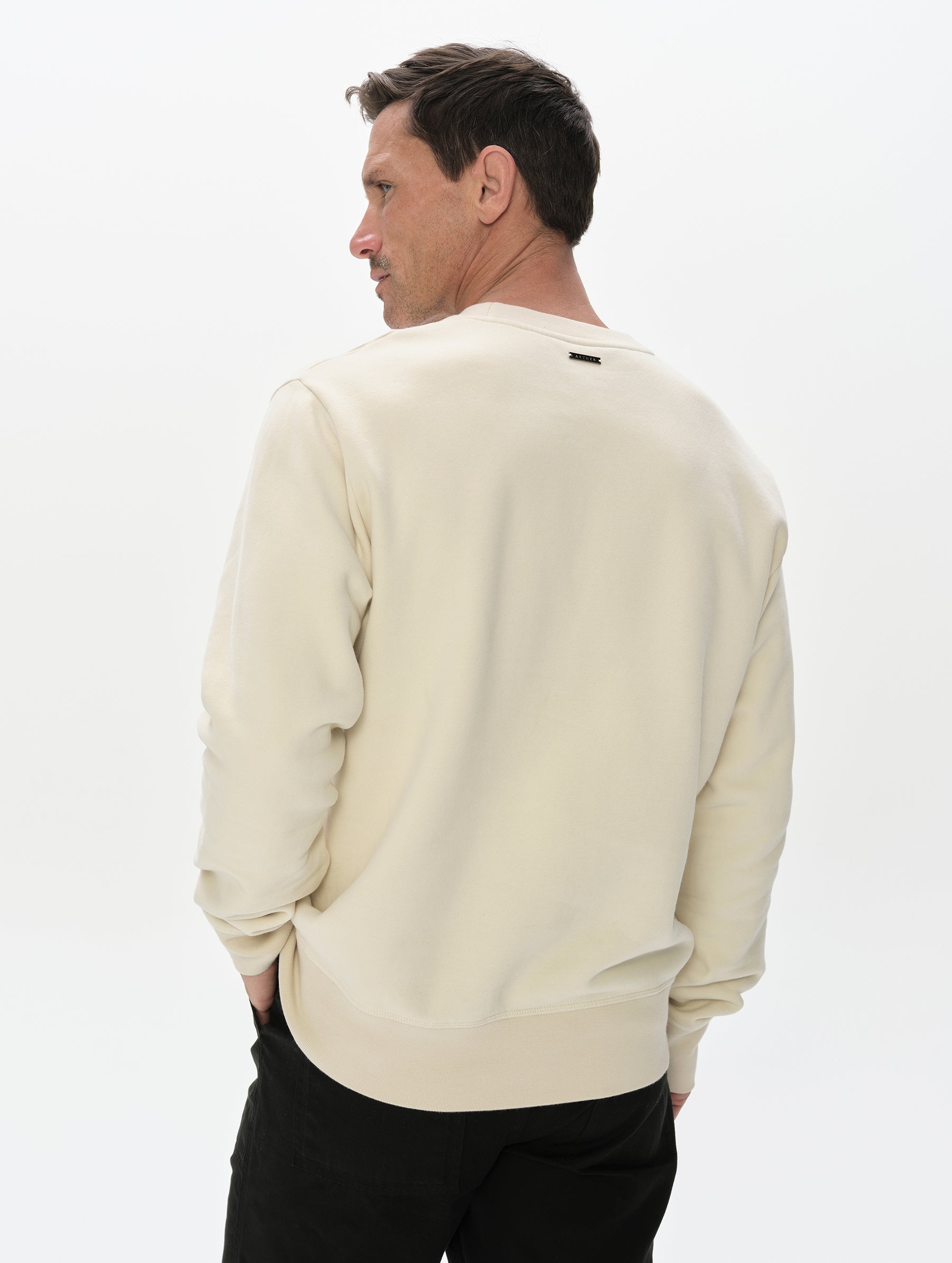 Rear, upper-body view of man wearing the Rylan Crewneck Sweatshirt in Bone from AETHER Apparel.