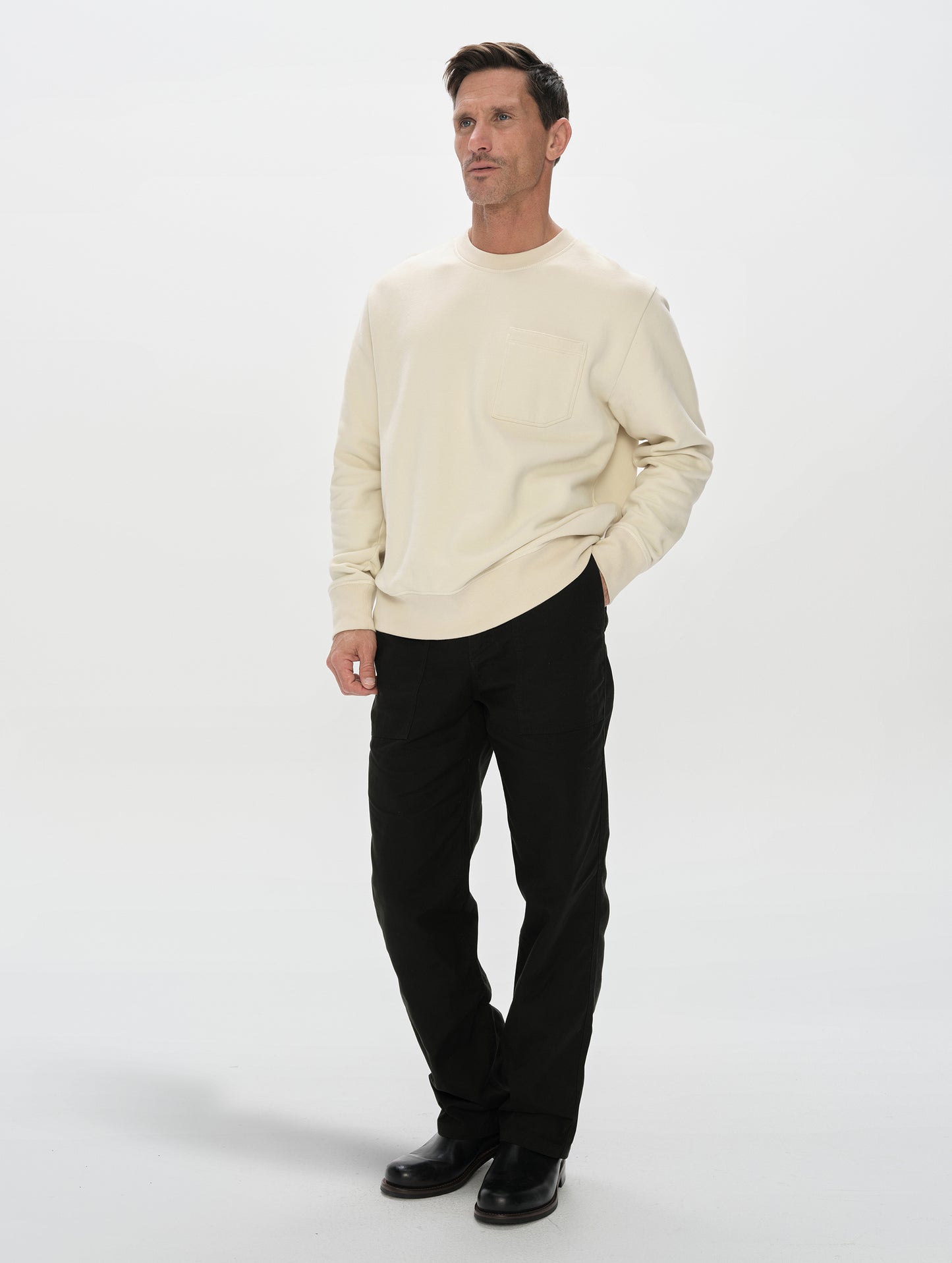 Front, 3/4, full-body view of man wearing the Rylan Crewneck Sweatshirt in Bone from AETHER Apparel.