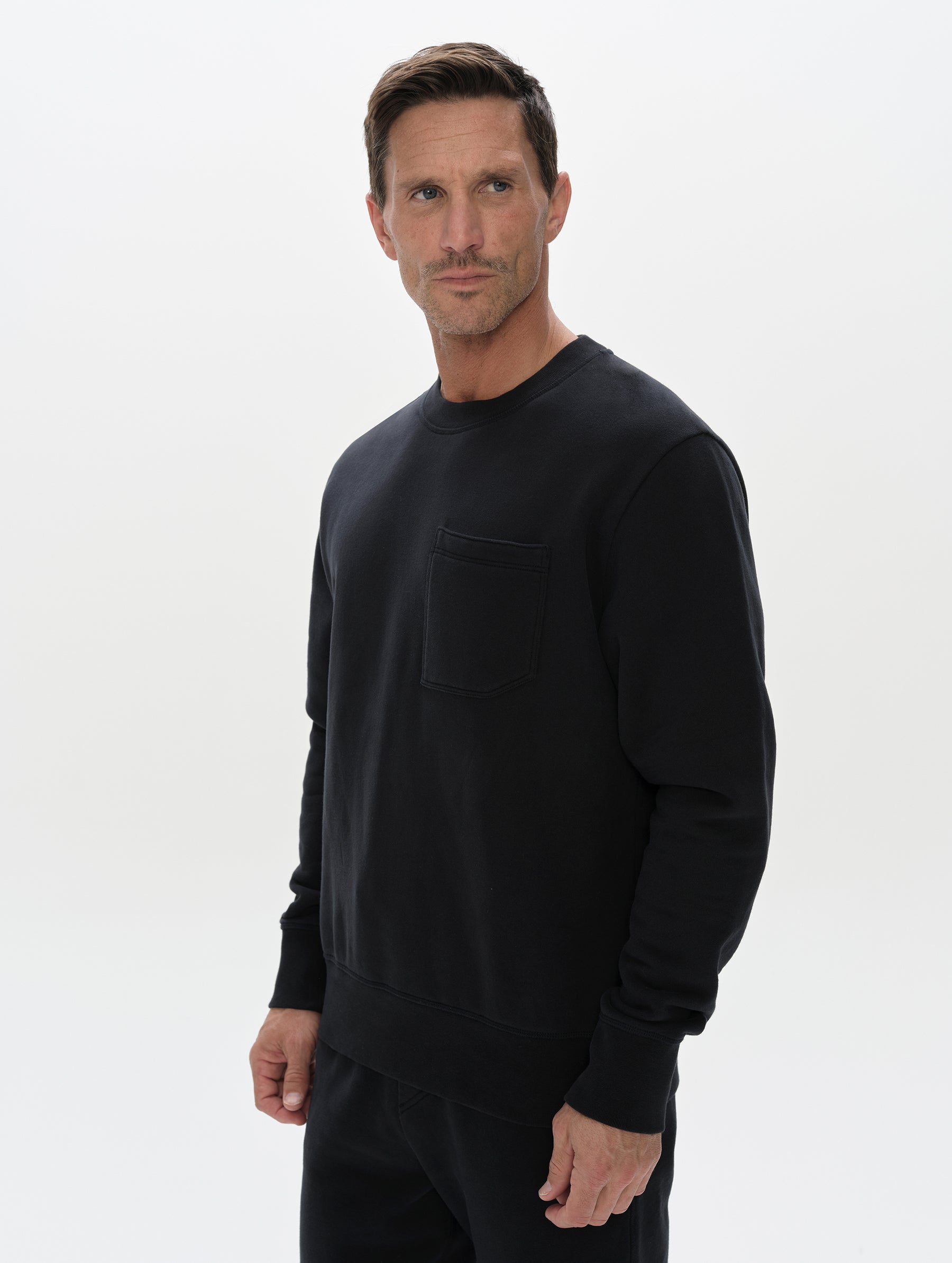 Front, 3/4, upper-body view of man wearing the Rylan Crewneck Sweatshirt in Onyx Black from AETHER Apparel.