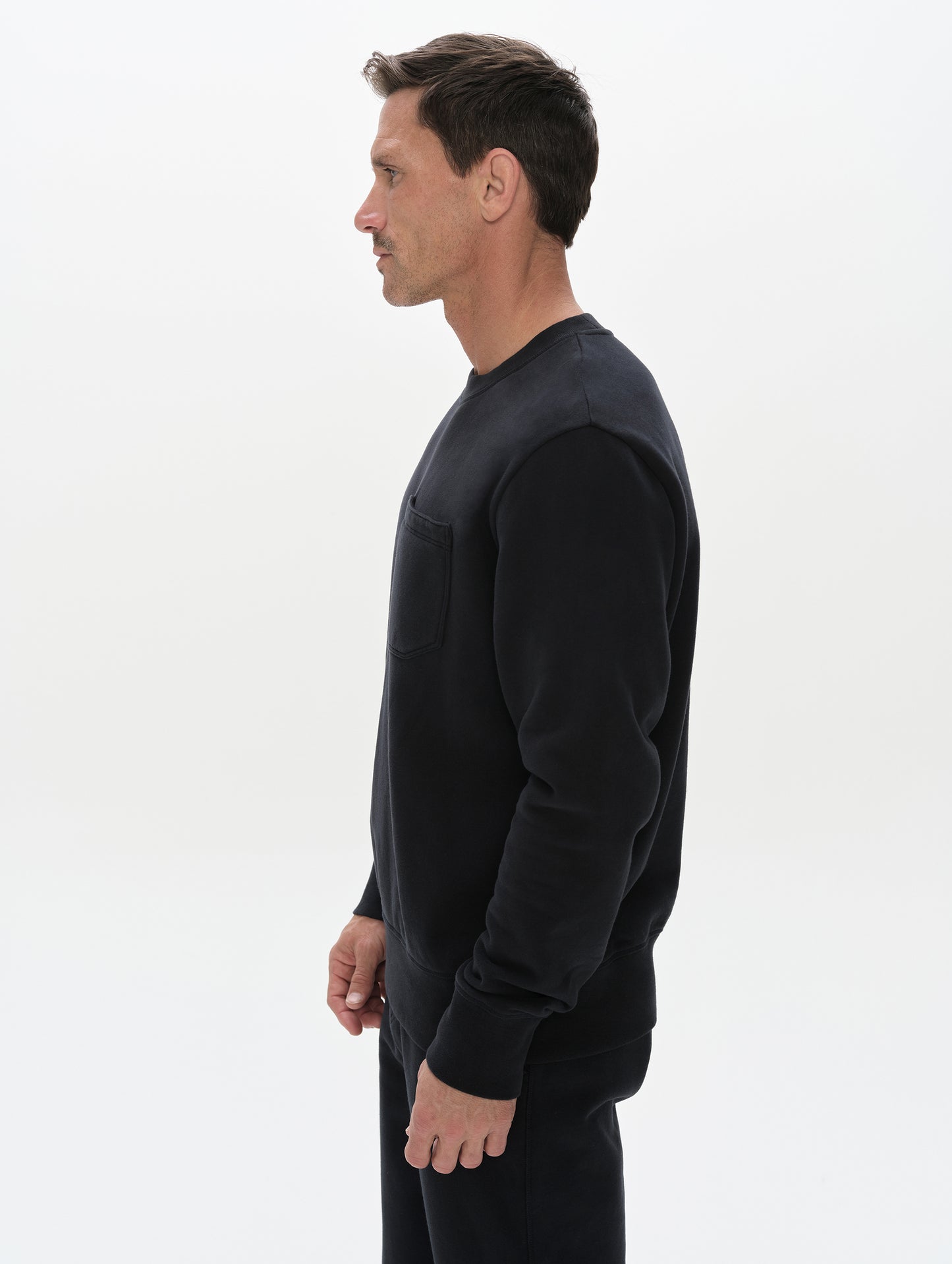 Side profile, upper-body view of man wearing the Rylan Crewneck Sweatshirt in Onyx Black from AETHER Apparel.