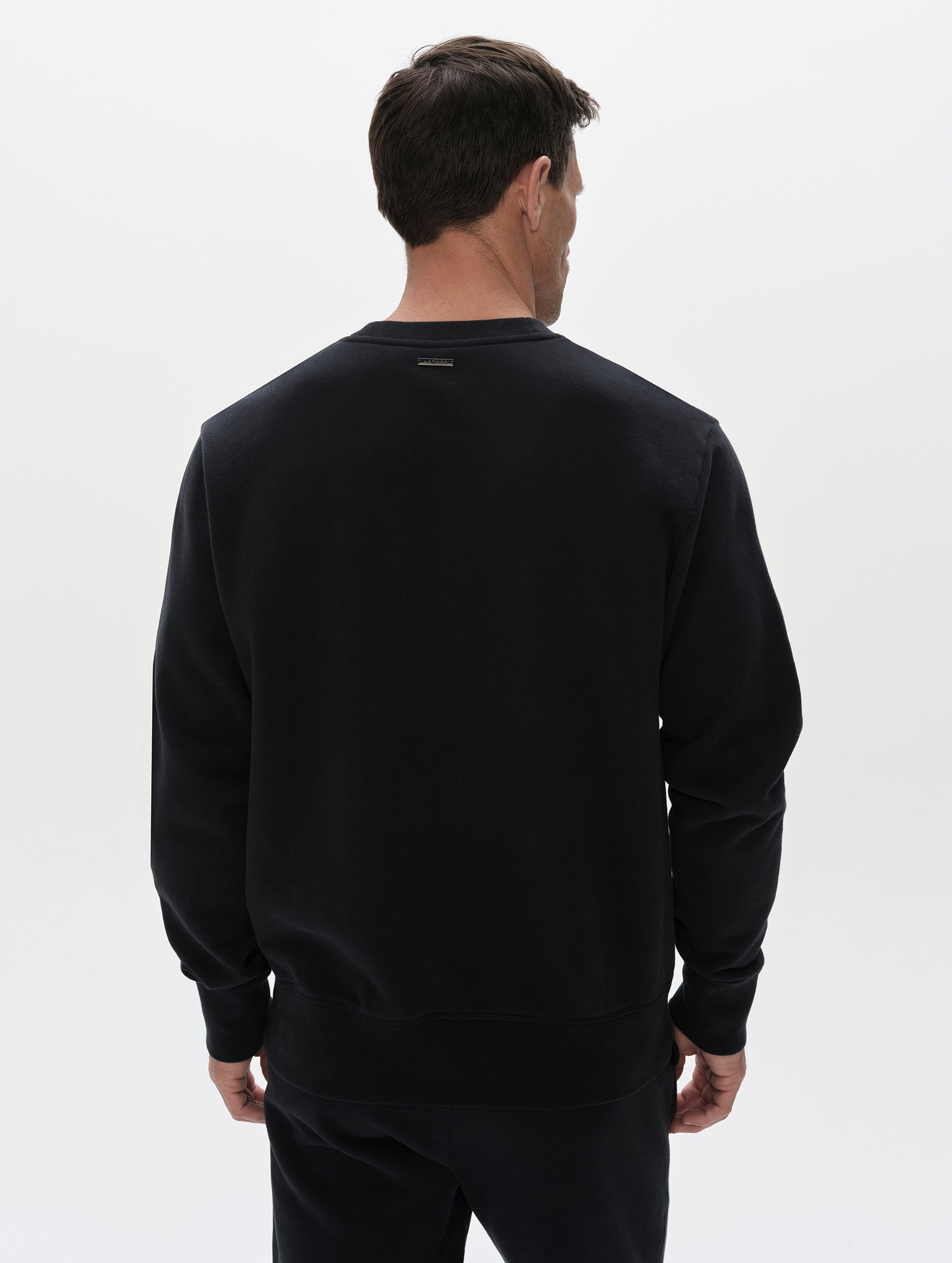 Rear, upper-body view of man wearing the Rylan Crewneck Sweatshirt in Onyx Black from AETHER Apparel.